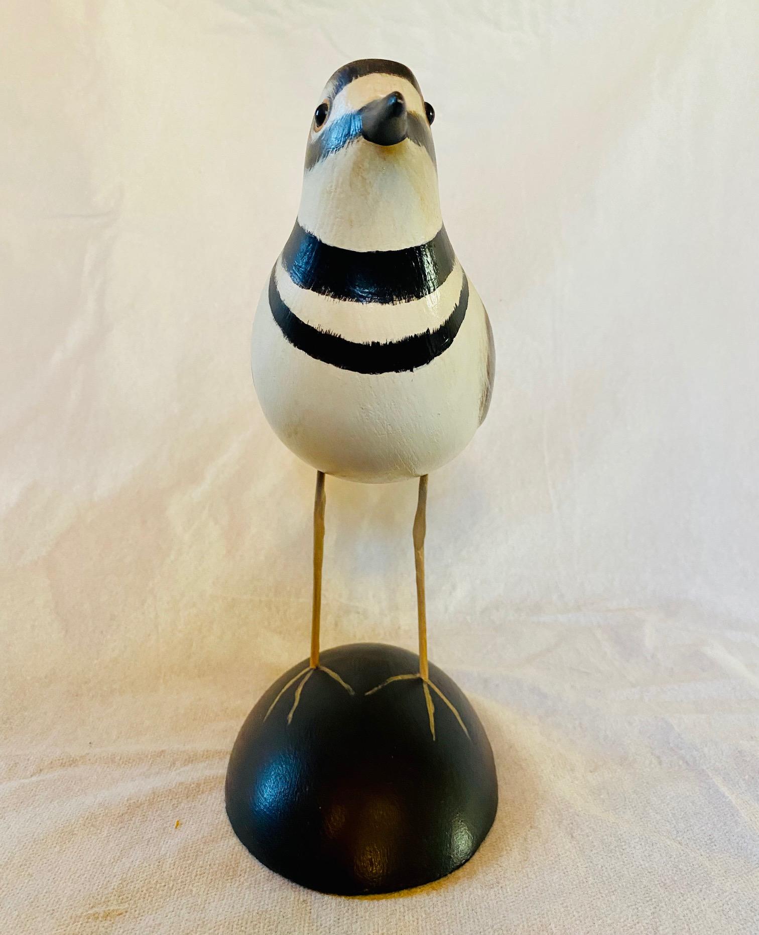 Carved and Polychromed Killdeer by Pat Gardner, Nantucket, 1973, a carved wooden alert shorebird with delicately painted plumage, glass eyes and wire legs, mounted on an ebonized domed base with painted feet, signed and dated on the belly, and
