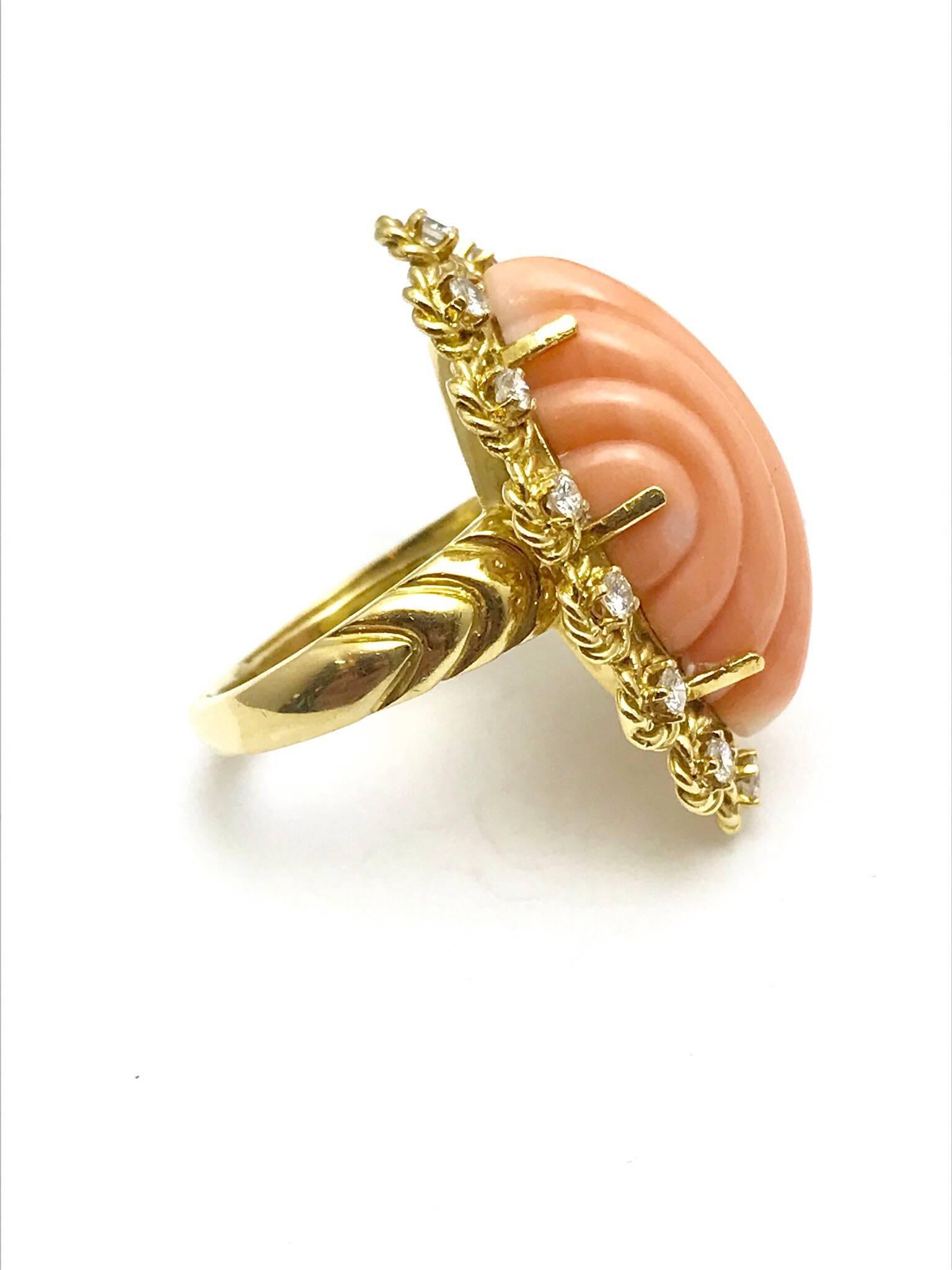 A carved angel skin coral and round brilliant diamond 18 karat yellow gold cocktail ring.  The coral is a carved cabochon marquise shape set with six prongs, framed by a single row of diamonds in a floral pattern.  The coral is 25.50 x 12.20 x