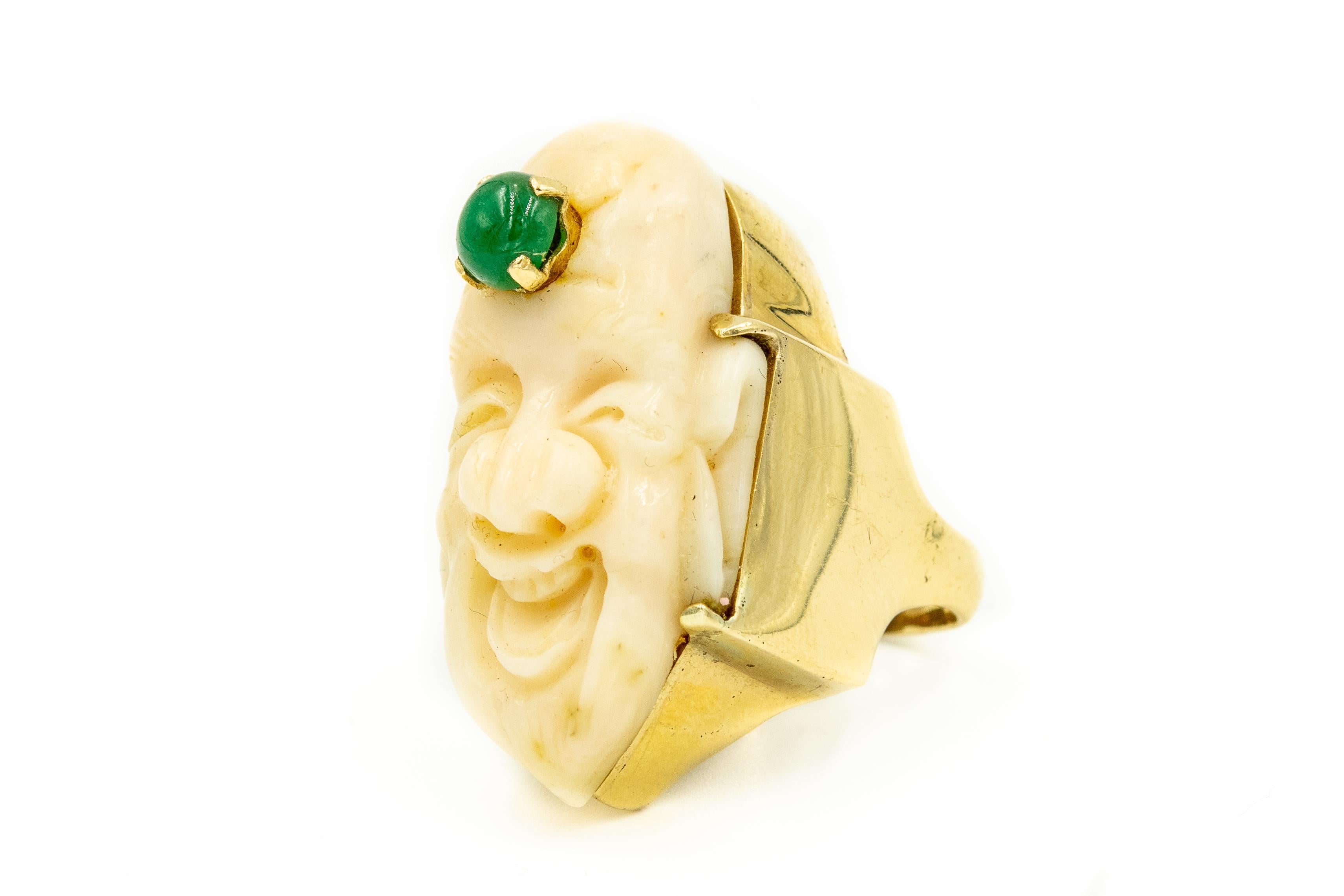 This joyful smiling Buddha is carved out of angel skin coral with a prong set emerald urna (the circular dot) on his forehead.  This lovely carving was then mounted in a custom handmade 14k yellow gold ring. 

 It is a size 6.5  US.

From Buddha