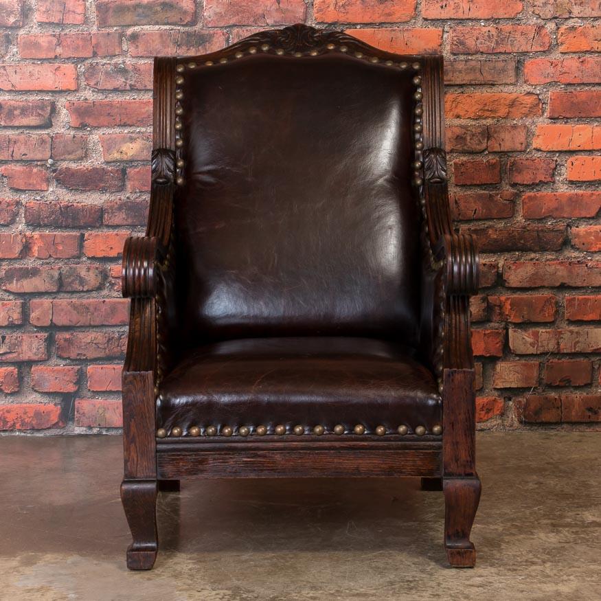 This impressive club chair is both handsome and comfortable. The heavy scrolled arms and carving are style elements from the early 1900s, Denmark. This arm chair has been recently reupholstered and covered in a dark reddish brown leather with large