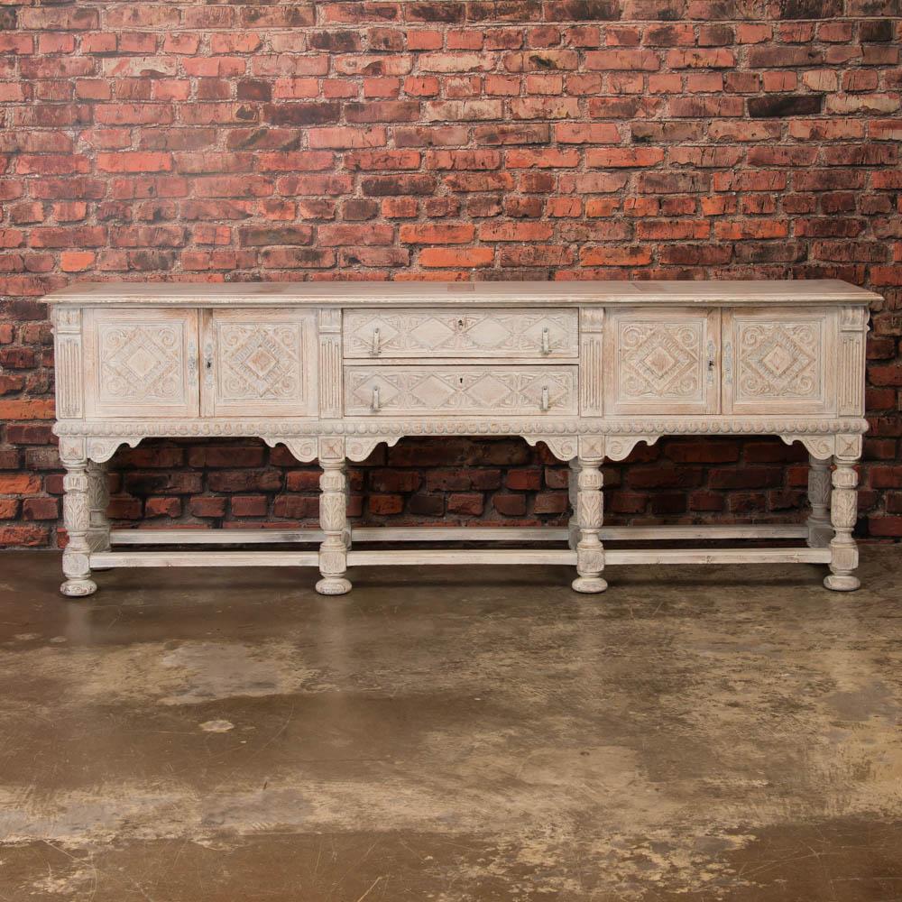 This antique oak sideboard or buffet from Sweden has been recently painted an off white that has been lightly scraped and sanded, exposing the natural wood beneath and highlighting the finely carved molding and panels of each drawer and door. Behind