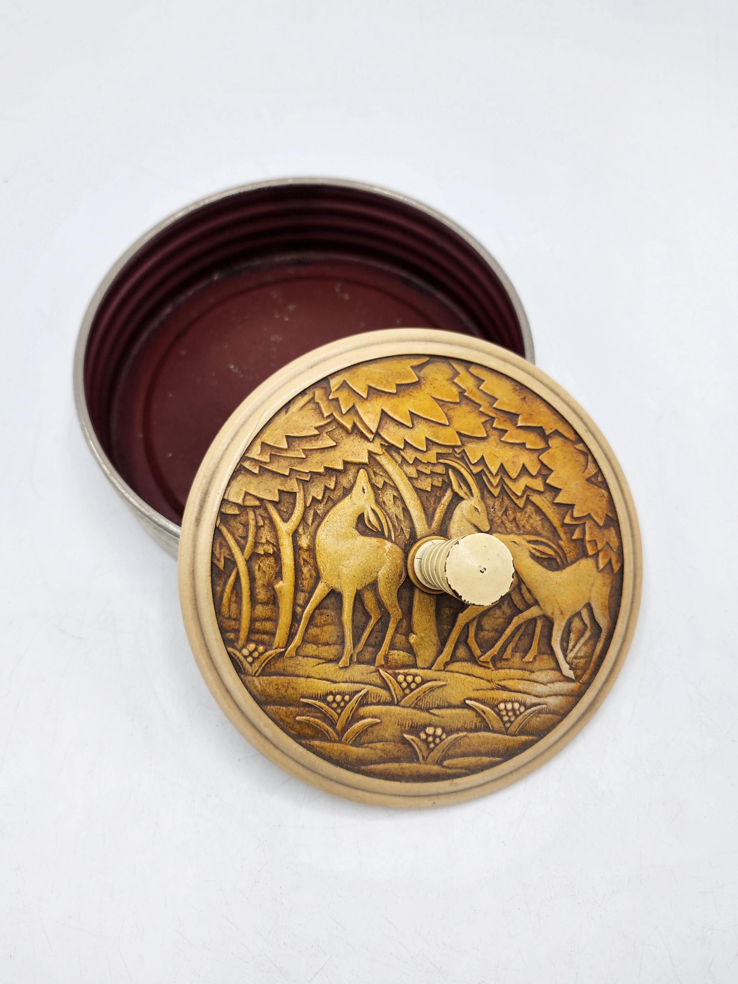 Carved Art Deco Decorative Box
This Art Deco decorative box features a cylindrical shape with a silver-plated metal base and a Bakelite or resin lid in shades of cream and brown. The lid is intricately carved with a design evoking a woodland scene,