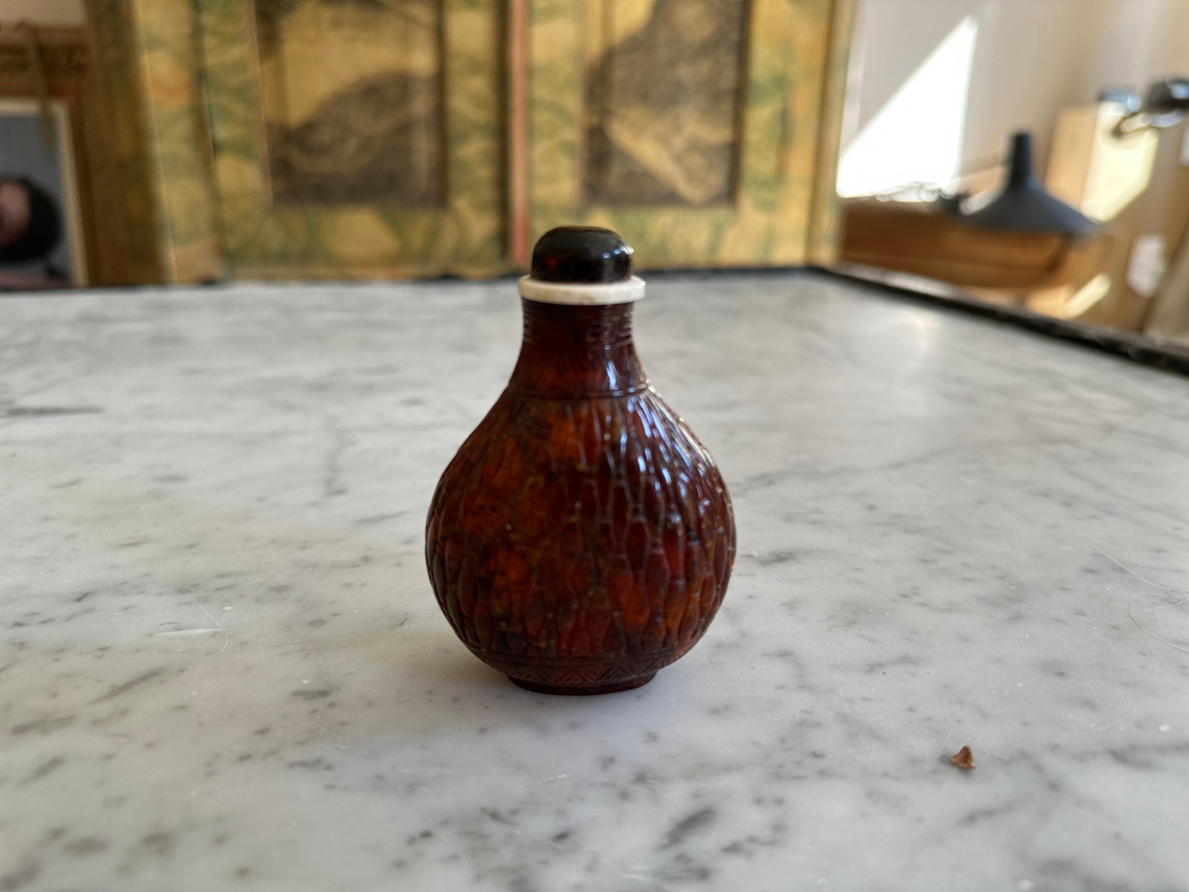 ntroducing our exquisite Asian Snuff Bottle, a true masterpiece crafted from the finest amber. This captivating piece boasts intricate relief carvings on its surface, showcasing the skilled craftsmanship of our artisans. The amber body of the bottle