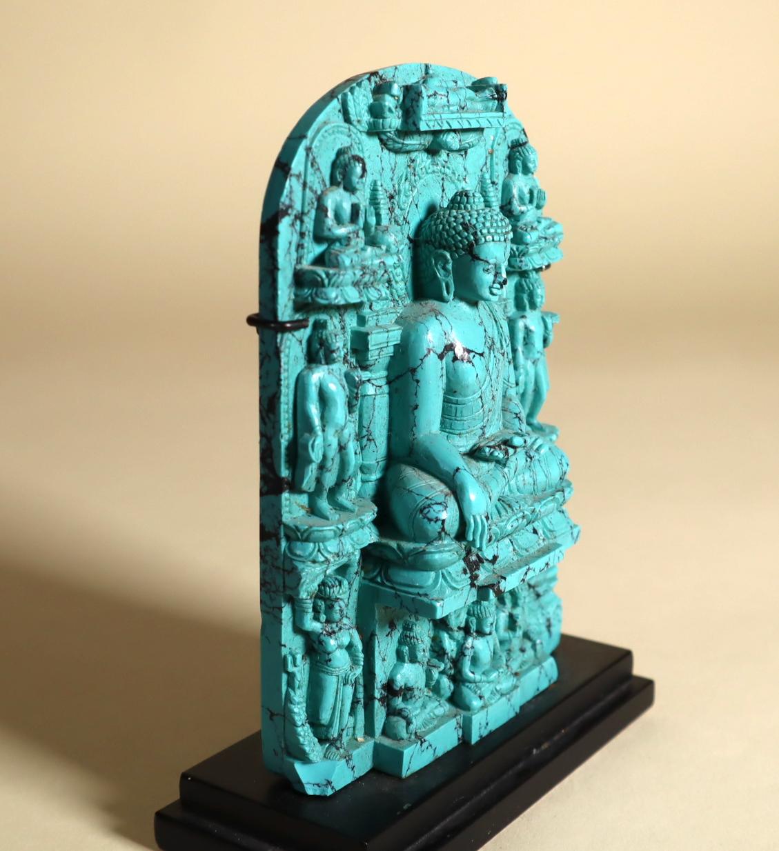 A finely detailed plaque of carved and polished turquoise depicting the life of the Buddha. South Asia. 20th century. 4.50 x 3 x 3/4 inches. With a custom metal stand that also has a wall mount option. Height of stand is 1/2 inch. 
Provenance: