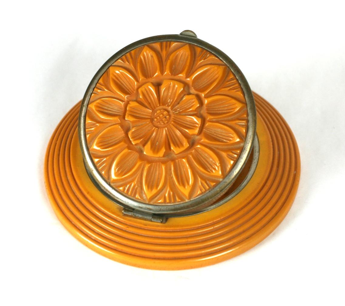 Carved Bakelite Art Deco Compact of finely carved and ribbed, butterscotch bakelite with concentric rings and a focal deeply carved blooming daisy. Chrome fittings with mirror and original powder puff.
Excellent Condition.   3.5