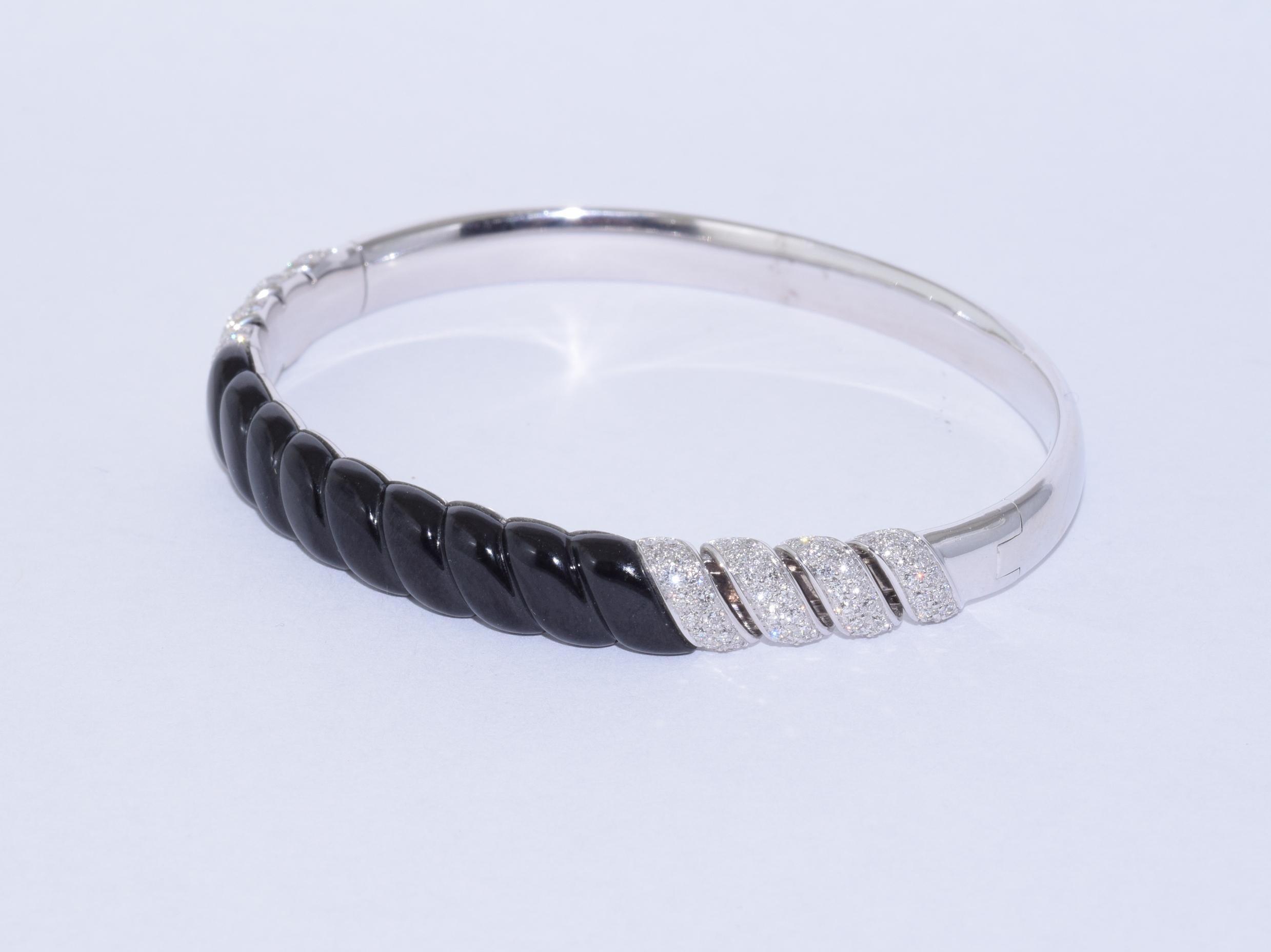 A hinged bangle topped with a carved black jade torsade shape is accented with round diamonds totaling approximately 1.11 carats mounted in 18 karat white gold. The bangle measures approximately 0.3 inch wide, with interior dimensions of 2.25in x