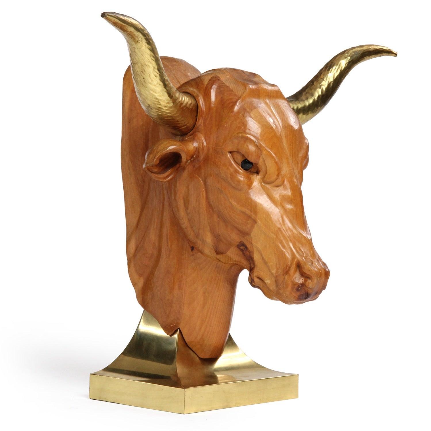 Escultura de madera tallada, detallada y de tamaño natural de una cabeza de toro con cuernos de latón incrustados y montada sobre una base inclinada de latón lacado.