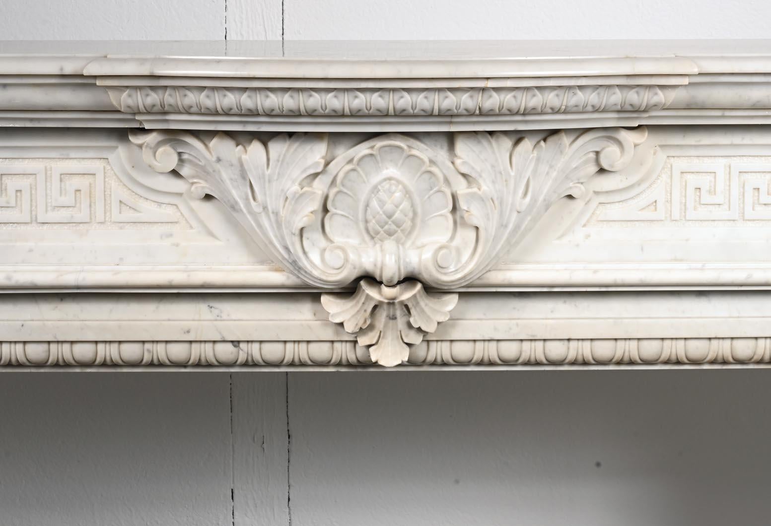 This Napoleon III style mantelpiece was created in Carrara marble in the 19th century. The centre of the lintel is adorned with a large plant pattern surrounding a stylized drawing of a flower. On both sides is a Greek frieze. The prominent