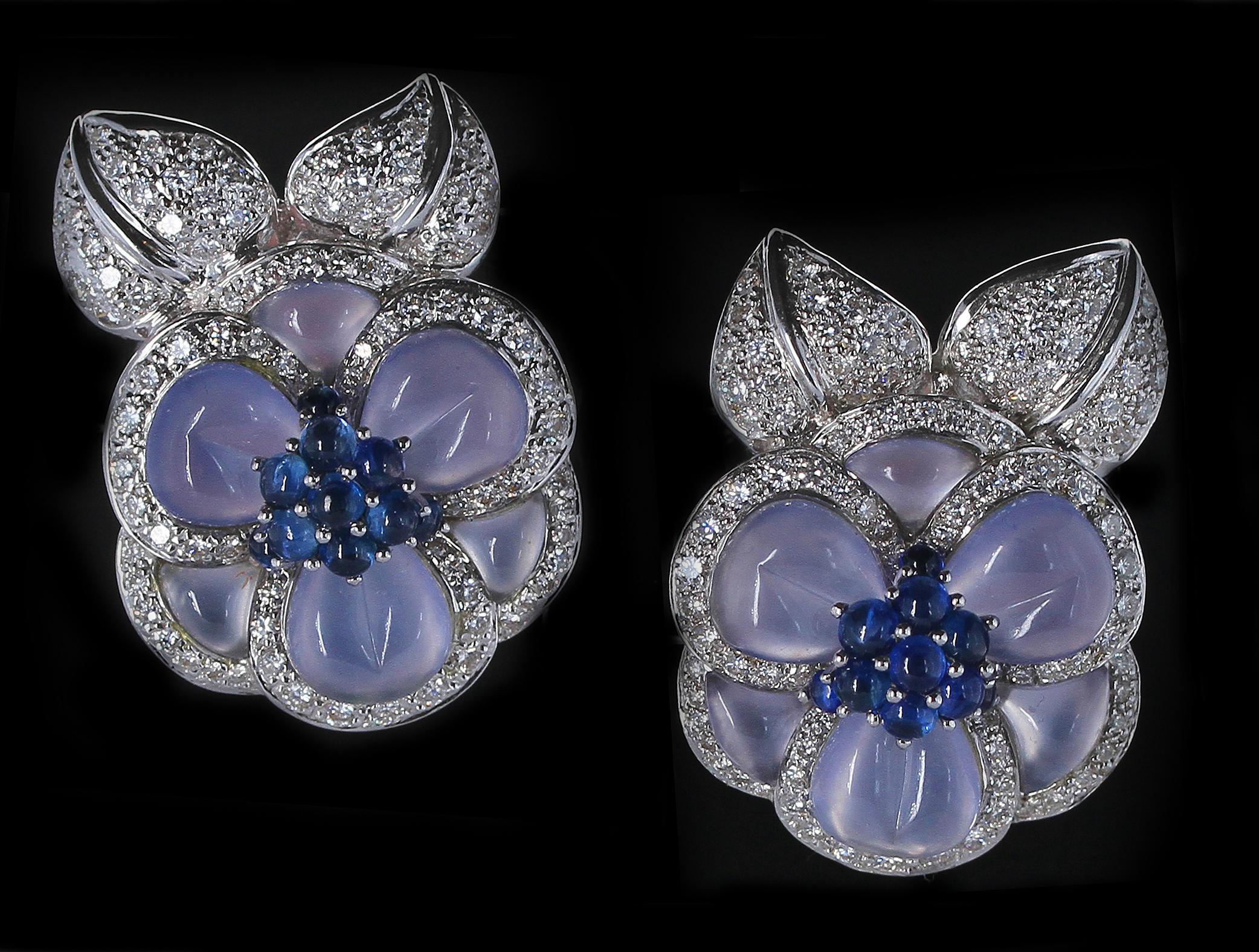 A stunning pair of carved chalcedony earrings accented with sapphire cabochons and diamonds. The chalcedony acts as petals and the sapphire cabochons are the pistil of the flower. The round diamonds are the leaves of the flowers. 18K White Gold. 1