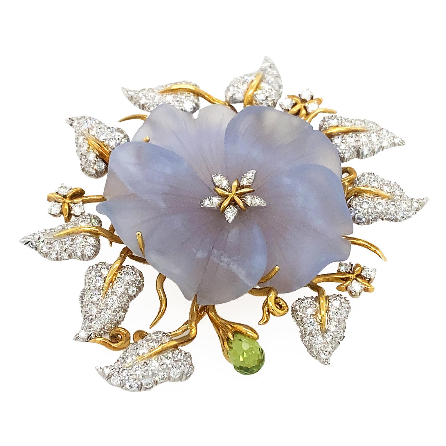 The delicate hued blue chalcedony illustrates a bloomed flower. The crystal is carved into overlapped petals with soft lines of texture, adding realism to the motif.  In between rays of 18k yellow gold are pear shape diamonds in the center. Behind