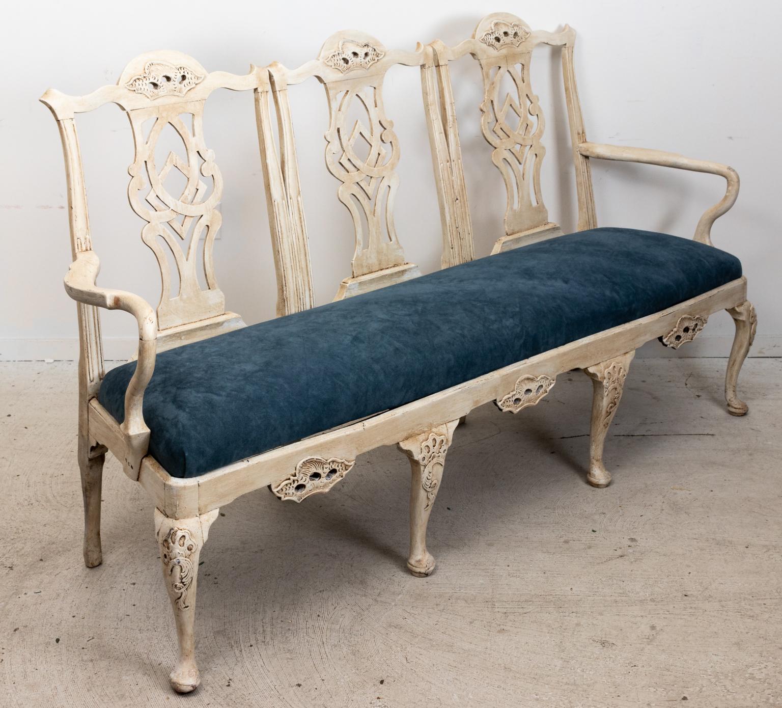 Painted settee in the Thomas Chippendale style with upholstered seat on cabriole legs with pad feet. The piece is further detailed with an ornately carved pierced back splat and bottom seat apron. The knees of the legs also feature scrolled motifs.