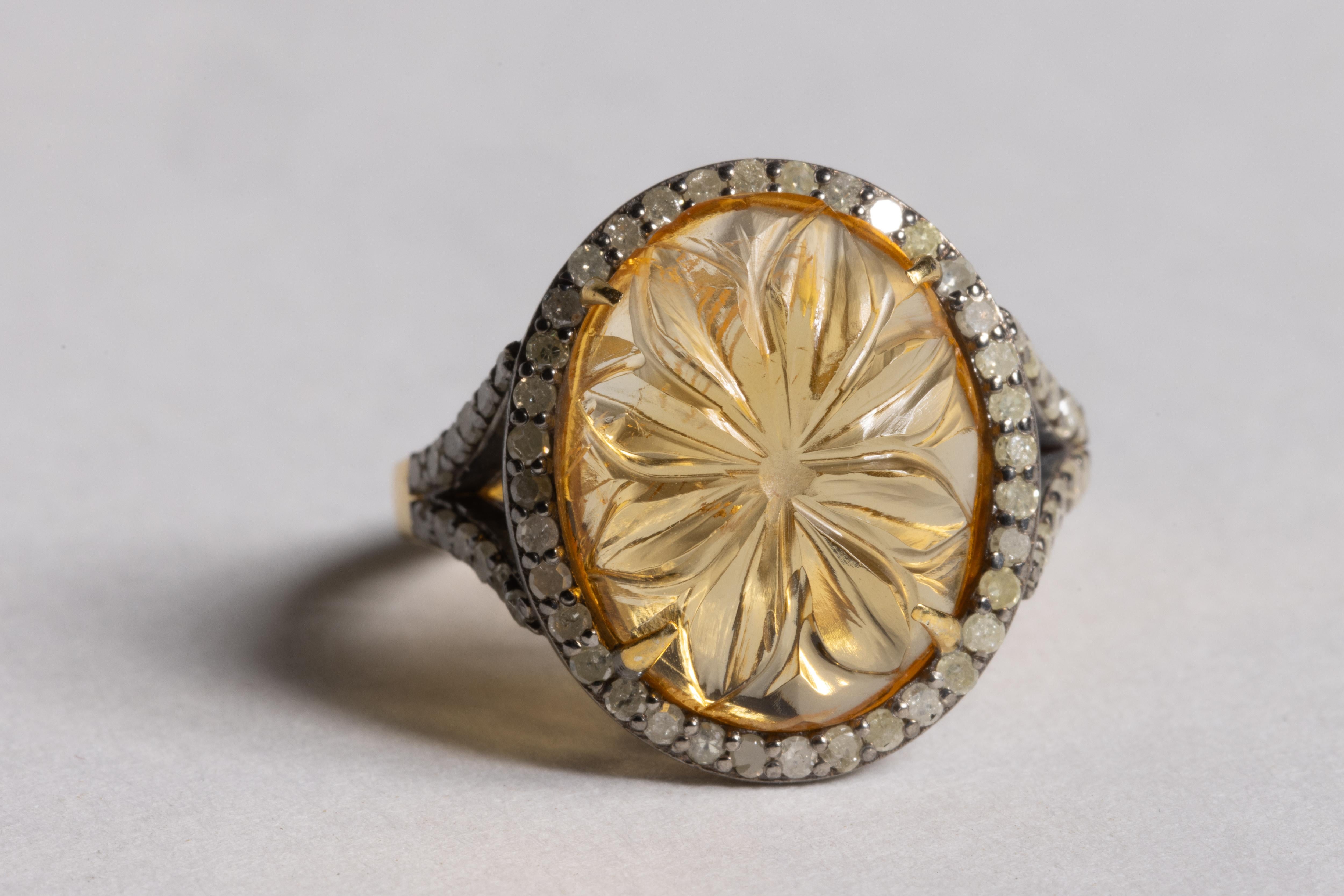 A carved oval citrine gemstone with a flower design, bordered with round, pave`-set diamonds.  Set in an oxidized sterling silver to set off the diamonds. and a vermeil band.  Citrine is 6.33 carats; and diamonds total .59 carats.  

The fine