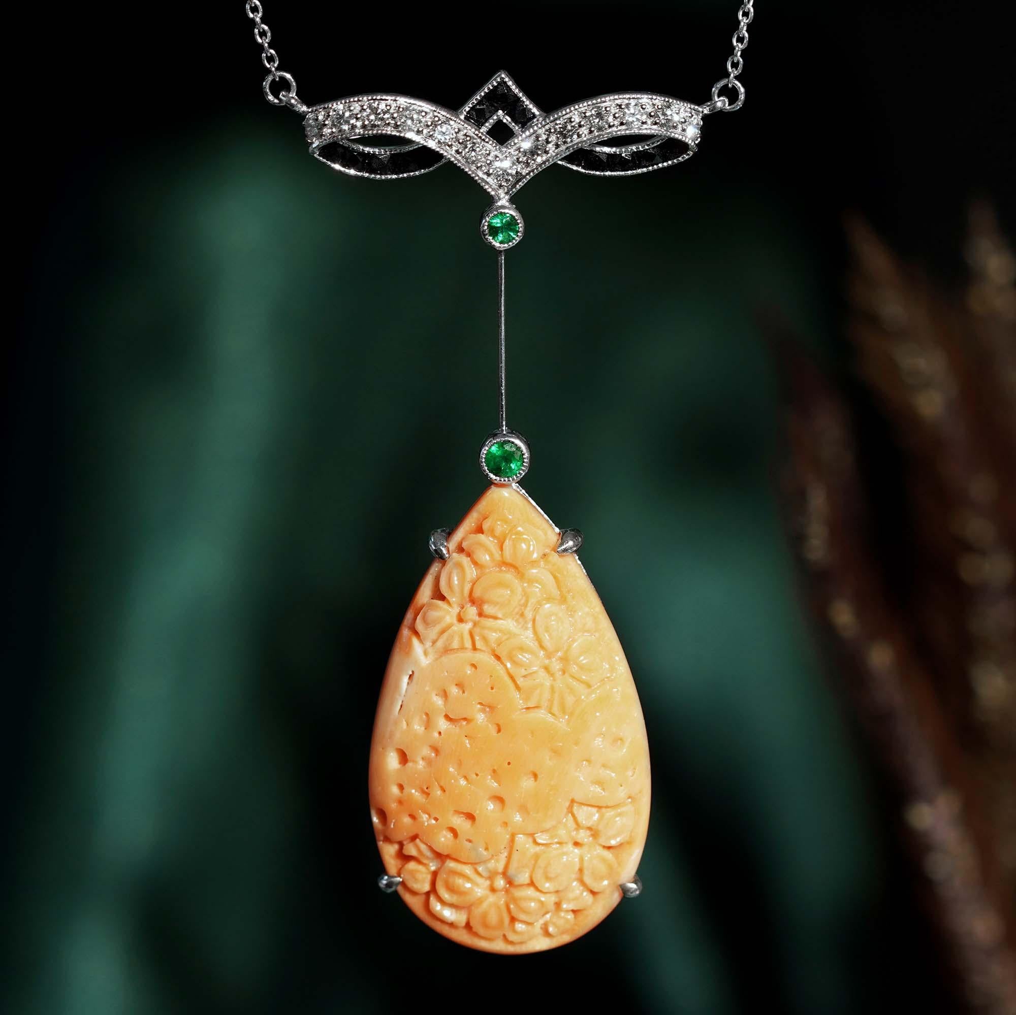 Un impresionante collar colgante de coral y diamantes de estilo Art Decó. Con un magnífico coral en forma de lágrima de aprox. 26,30 con motivo floral tallado. Engarzado bajo 2 esmeraldas redondas diminutas, el diamante y el giro de ónice negro en