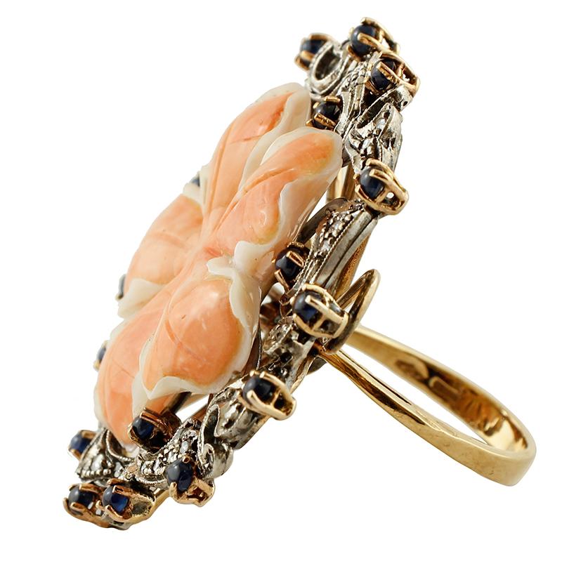 Vintage ring in 9k rose gold and silver structure, mounted with a central finely carved coral flower, surrounded by a flowery structure studded with diamonds and blue sapphires
The origin of this ring goes back to the 1980s, it was totally handmade