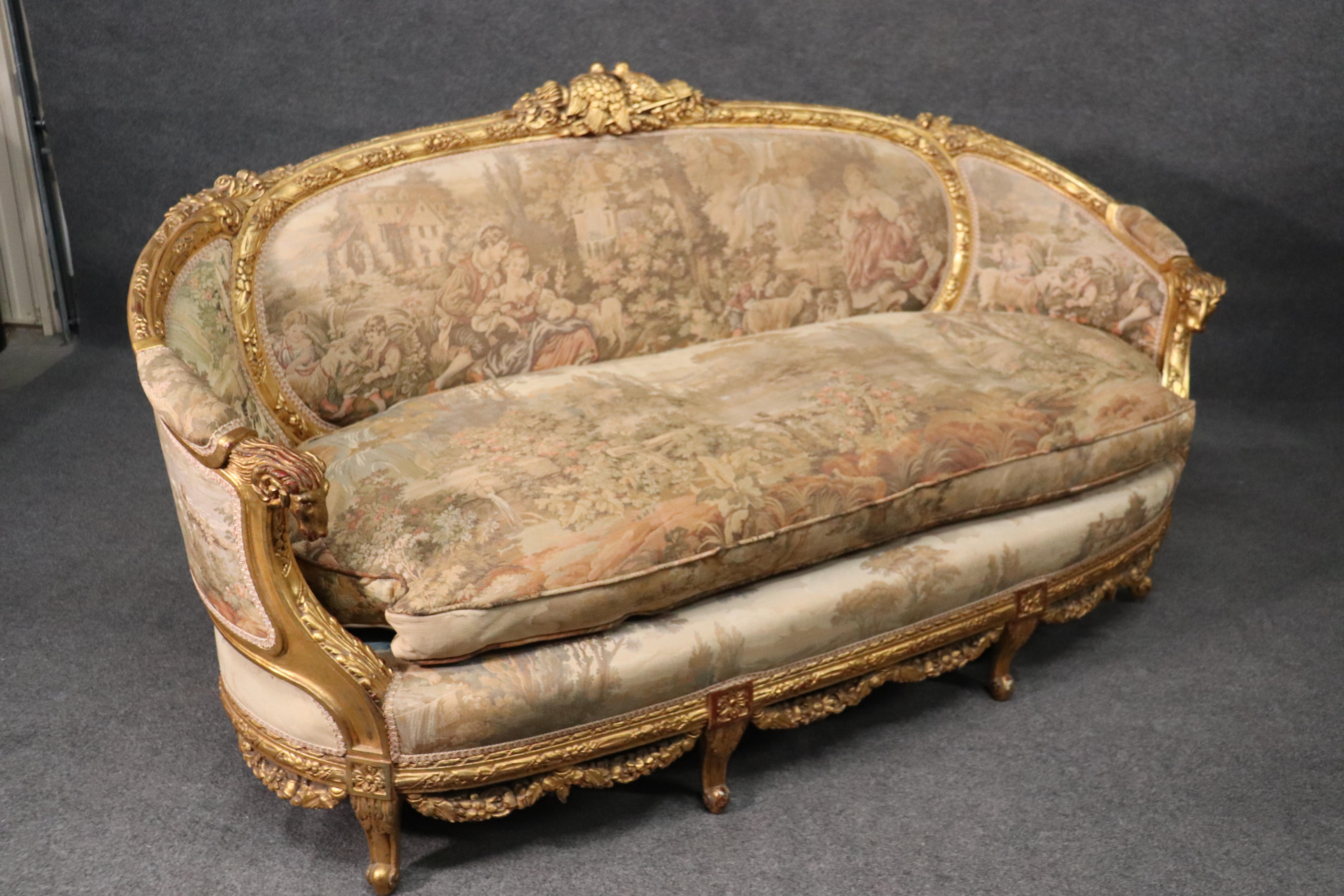 This is a fantastic sofa in genuine gold leaf over a red clay bole ground. The sofa is covered in a machine-made tapestry depicting courtship scenery and the usual French romantic themes. The sofa is in very good original condition and has no major