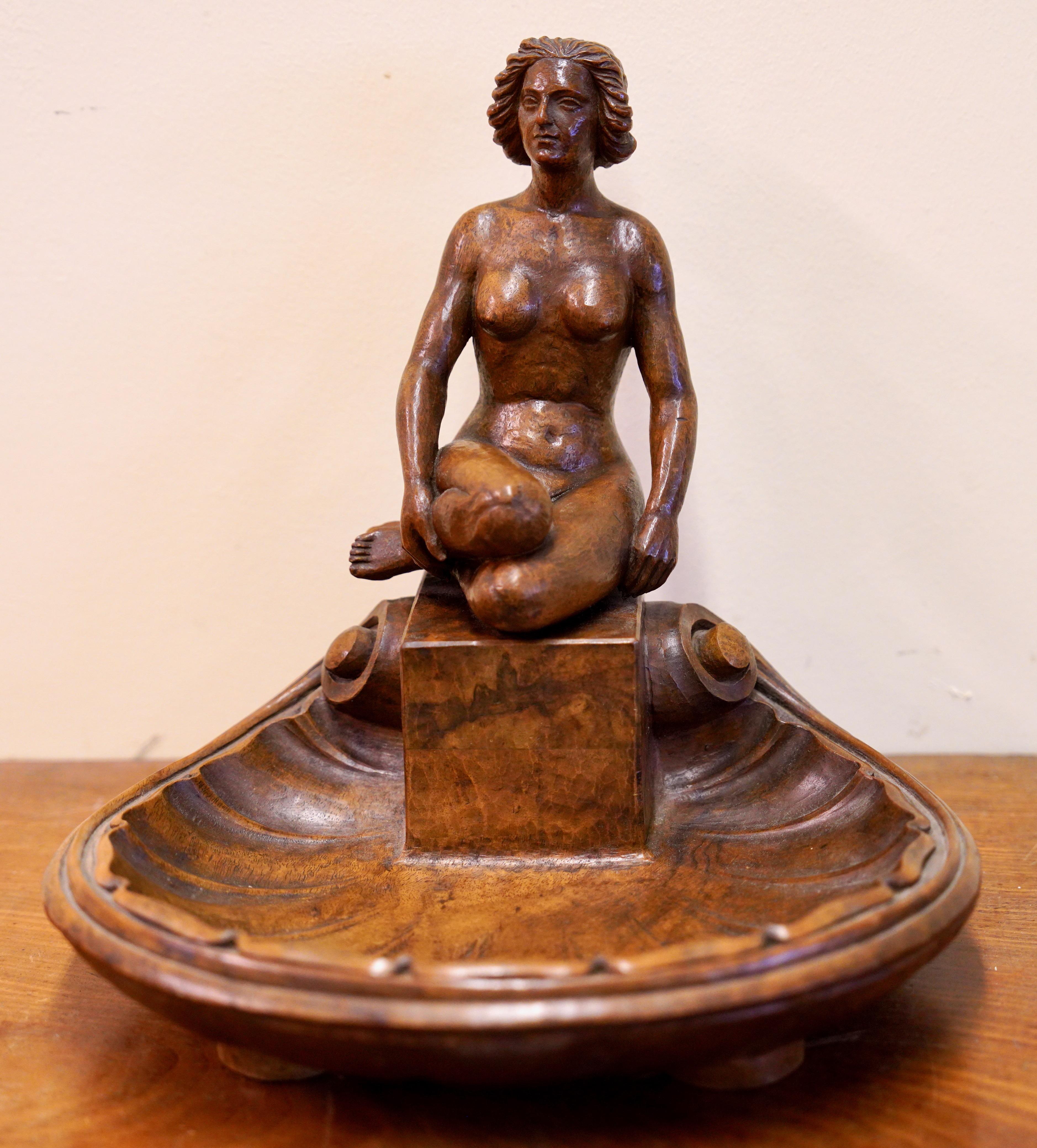 Geschnitzte dekorative Holzfigur, nackte Frau auf Muschel

Diese atemberaubende geschnitzte antike Holzfigur stellt eine nackte Frau dar, die auf einem stilisierten Sockel thront, der in eine Muschelform übergeht. Die künstlerische Darstellung und