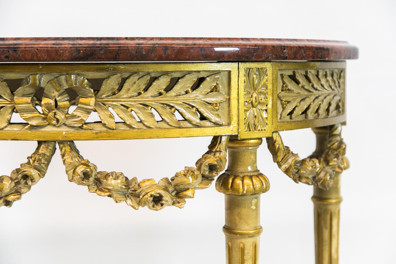 Carved demilune marble top console table is painted in gilt with reticulated ribbon and leaf carving. It has carved floral swags beneath the apron with fluted tapering legs with carved acanthus leaves at the base. There are carved leaf supports for