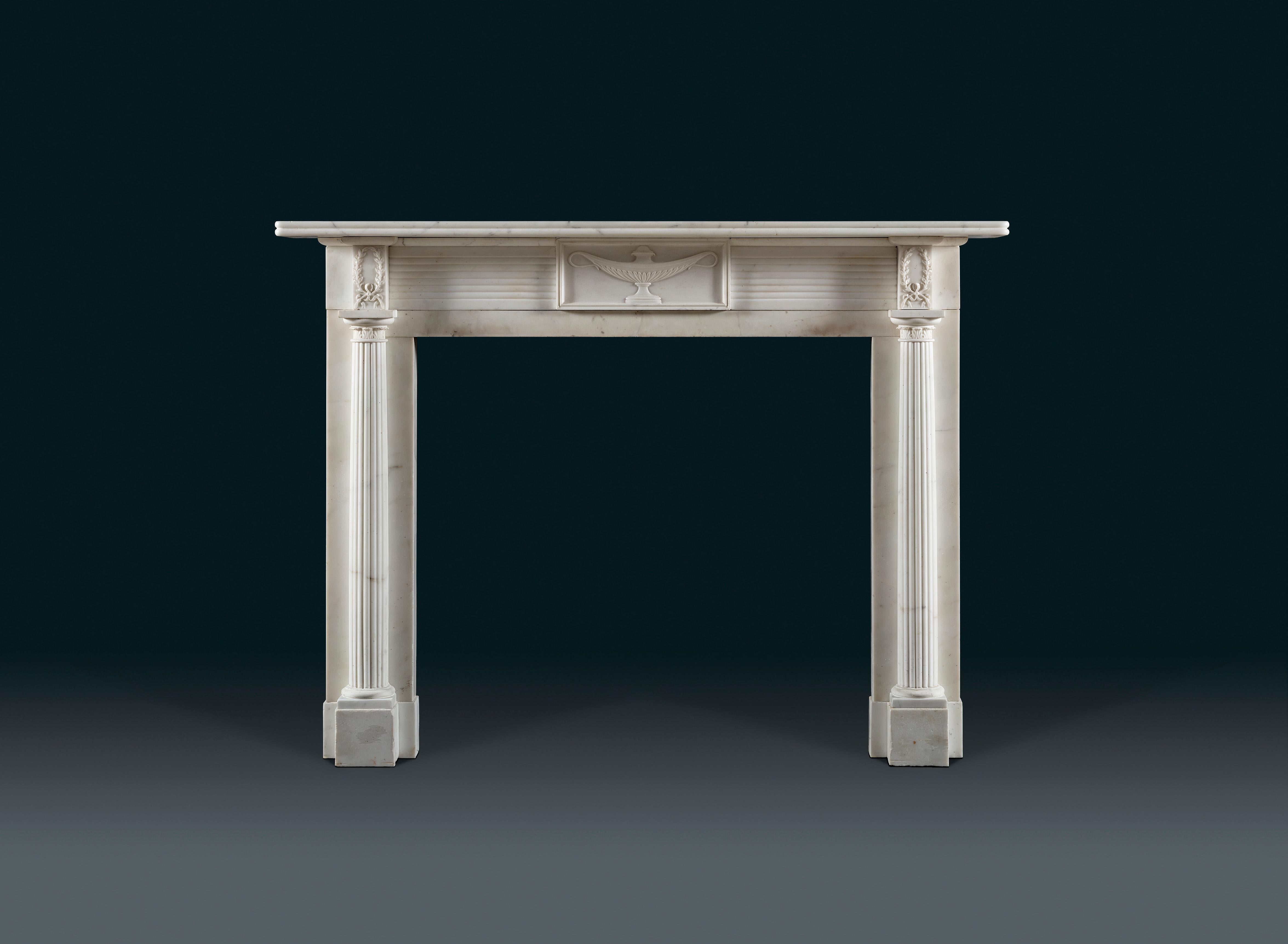 An exquisitely carved early 19th century Regency period chimneypiece in statuary white marble. The central tablet carved with a tazza urn, flanked by a reeded frieze and end blockings carved with delicate laurel wreaths, above engaged half column