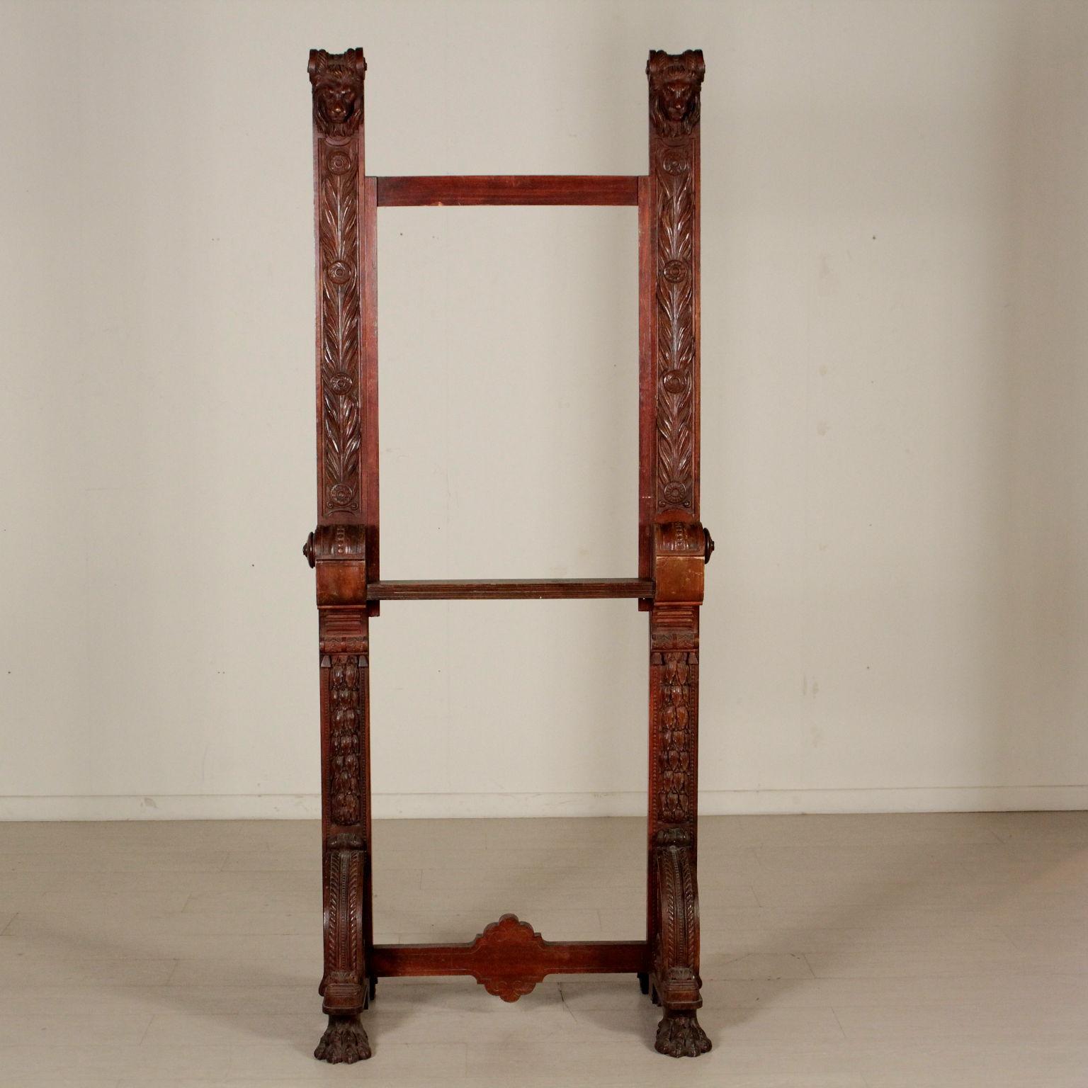 An impressive easel for paintings, finely carved. Ferine feet with volutes and crossbeams. Uprights with leaves culminating with leonine heads. Not adjustable ground plane. Manufactured in England, last quarter of the 19th century.