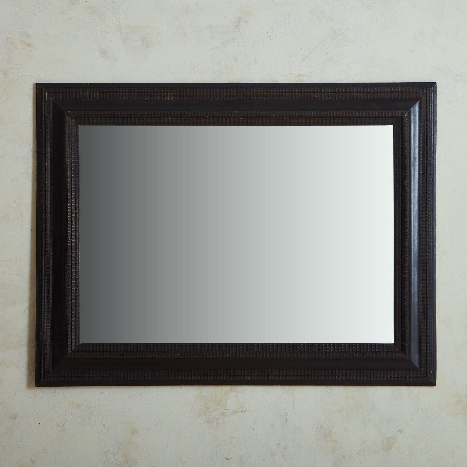 A vintage french wall mirror featuring a rectangular ebonized wood frame with intricate carved linear details. This piece has a wooden backing and hardware for hanging. Sourced in France, 20th Century.