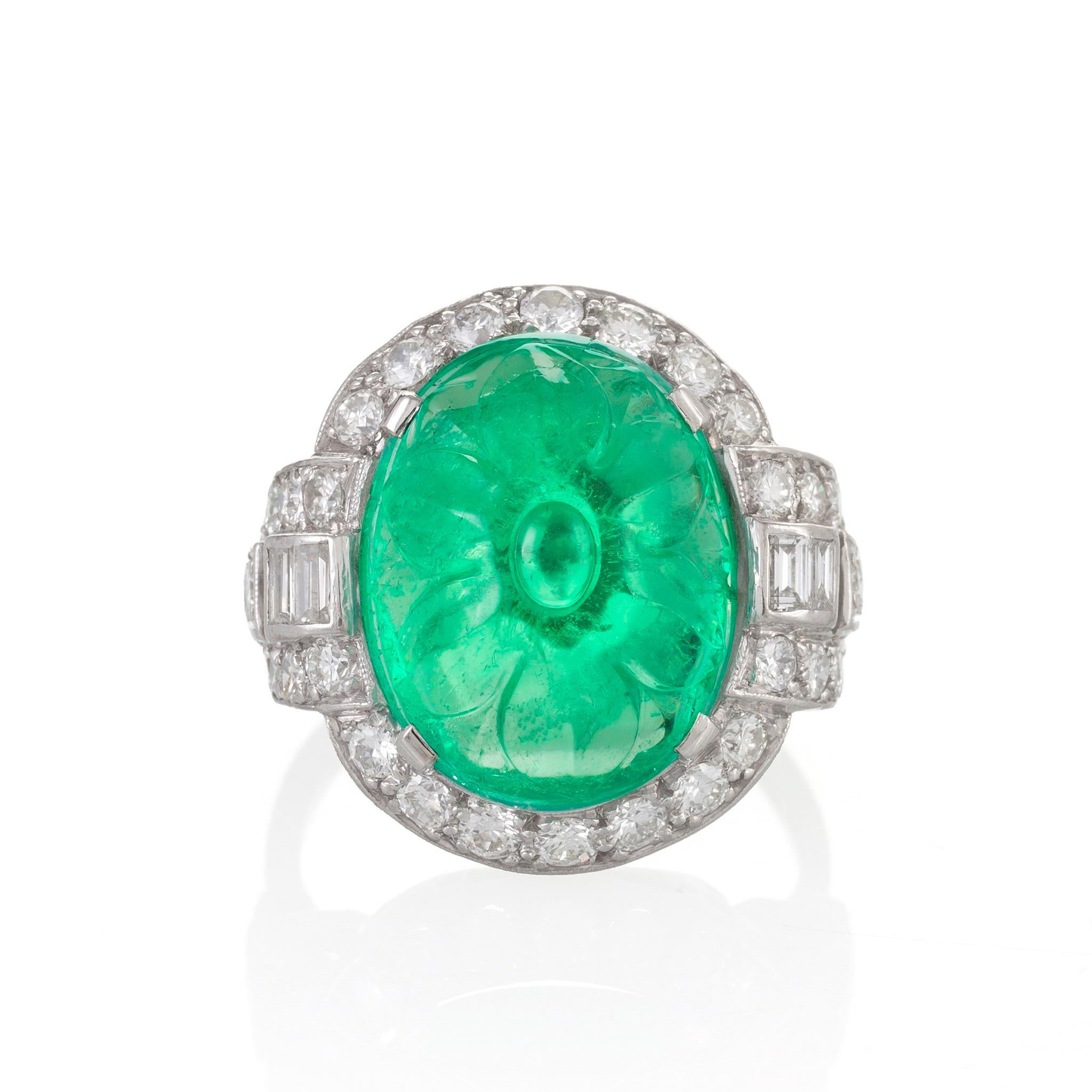 This colorful Art Deco platinum ring, dating from the 1920s, is set with a floral-carved emerald cabochon weighing over eight carats, framed by sparkling diamonds. The substantial emerald is carved as a blossoming flower with full and elongated