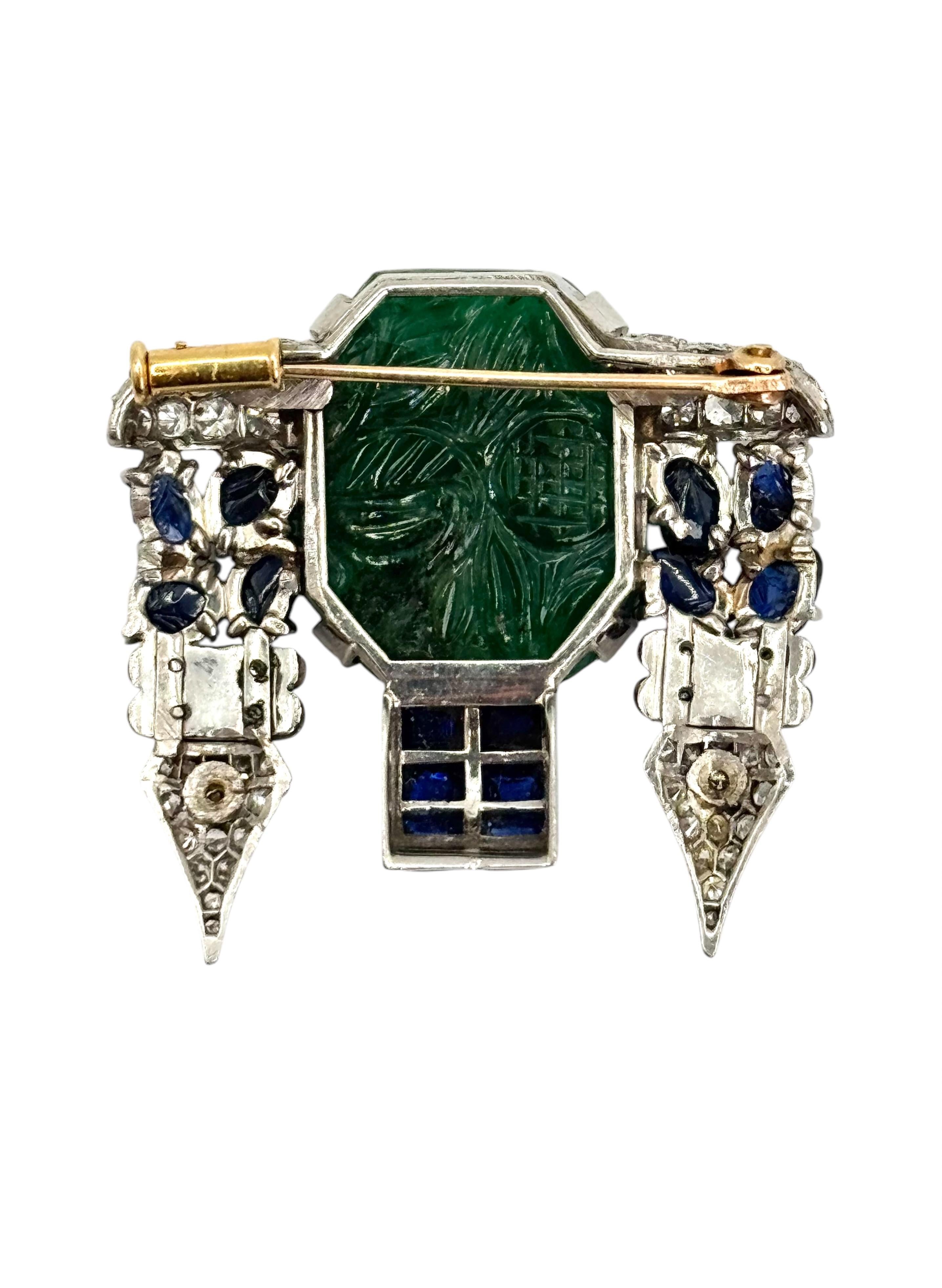 A striking unisex Art Deco brooch featuring a meticulously carved emerald centerpiece, flanked by carved sapphires and rich onyx accents. Set in platinum, the design is completed with brilliant-cut diamonds that bring dynamic contrast and sparkle. A