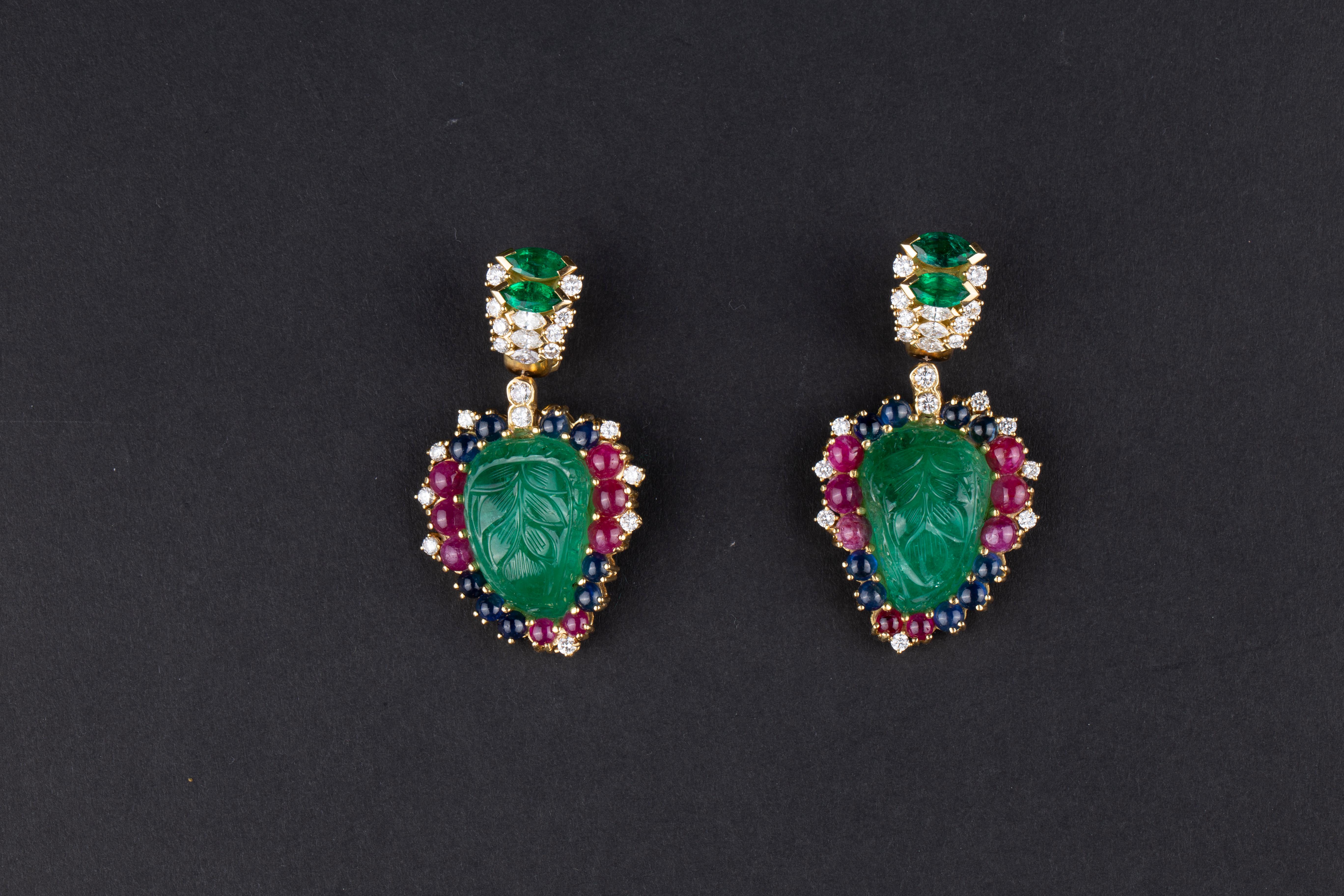 A pair of 18k yellow gold ear pendants suspending two carved emeralds (80cts total), marquise emeralds (2.5 carats total), diamonds (1.8 carats), rubies, and sapphires, ear-pendants. Made in Italy, circa 1980.