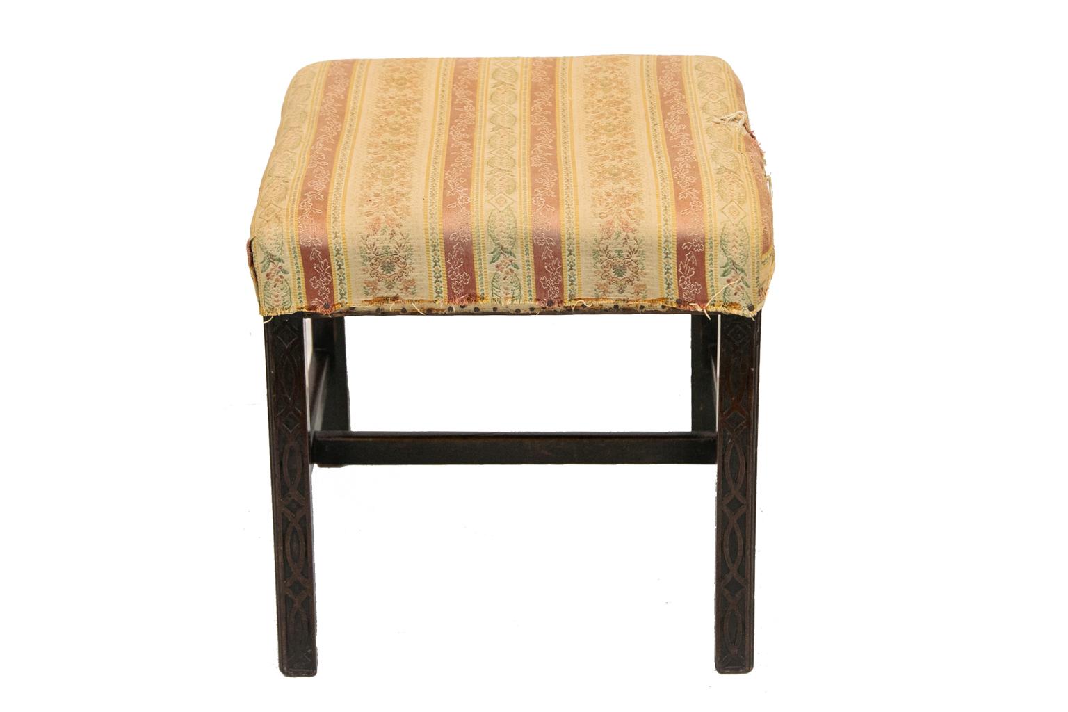 This carved English Chippendale stool has all of its original four glue blocks underneath with four 19th century reinforcements added. The legs are carved with beaded corners and interlaced blind fretwork on all eight sides. The legs are supported