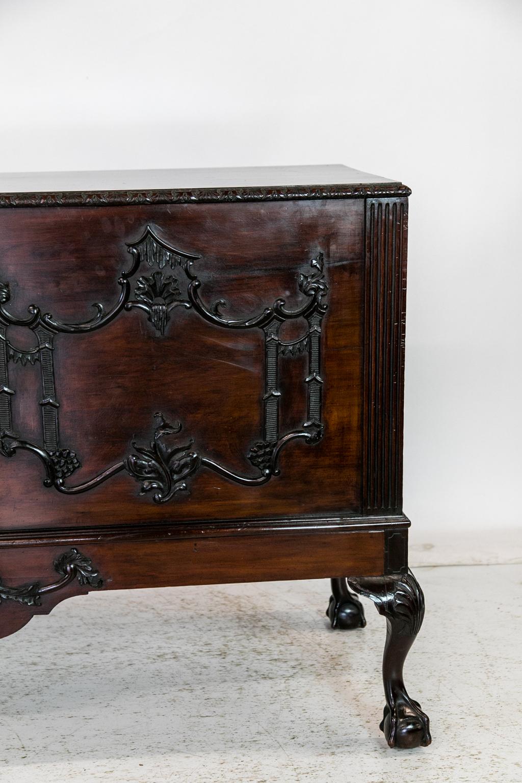 The top of this carved English mahogany blanket chest on legs has a carved edge with stylized scallop shells and waves. The front is carved with raised Rococo double cartouches. The bottom apron has a large stylized shell in the center. The legs