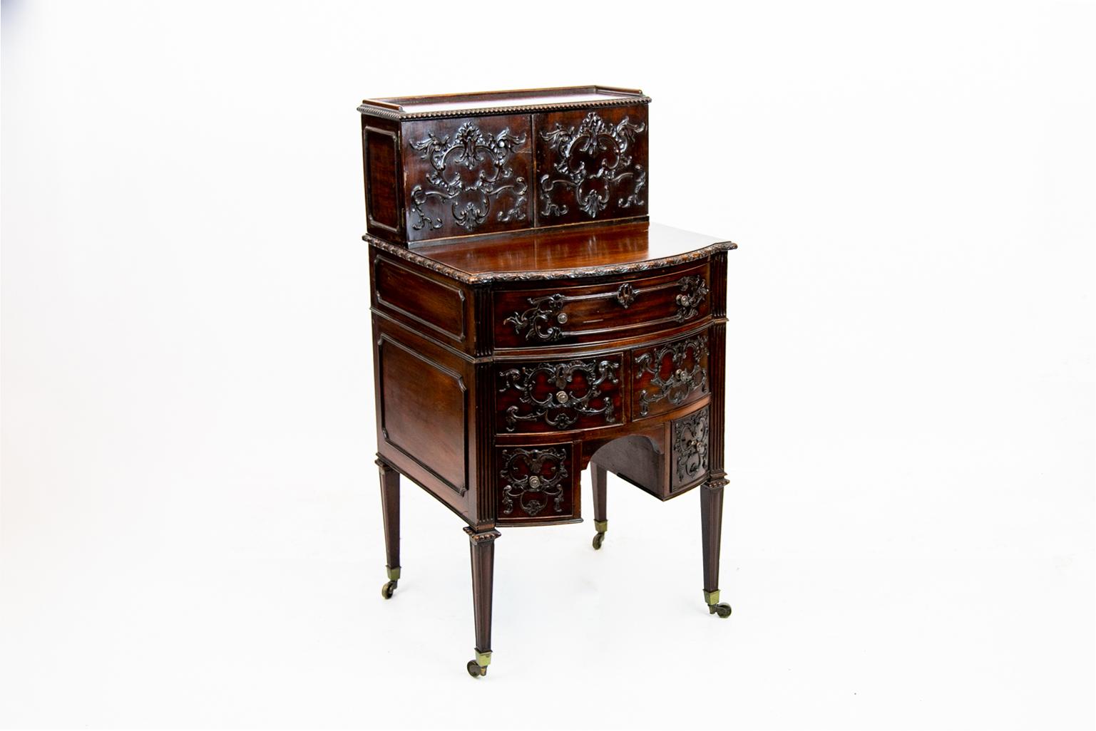 Carved English mahogany Hepplewhite bow front desk on legs. Top section with Rococo carvings, gadrooned top edges, and a shallow gallery. Two interior drawers with divisions. Bottom section has five drawers with Rococo carvings and fluted stiles,