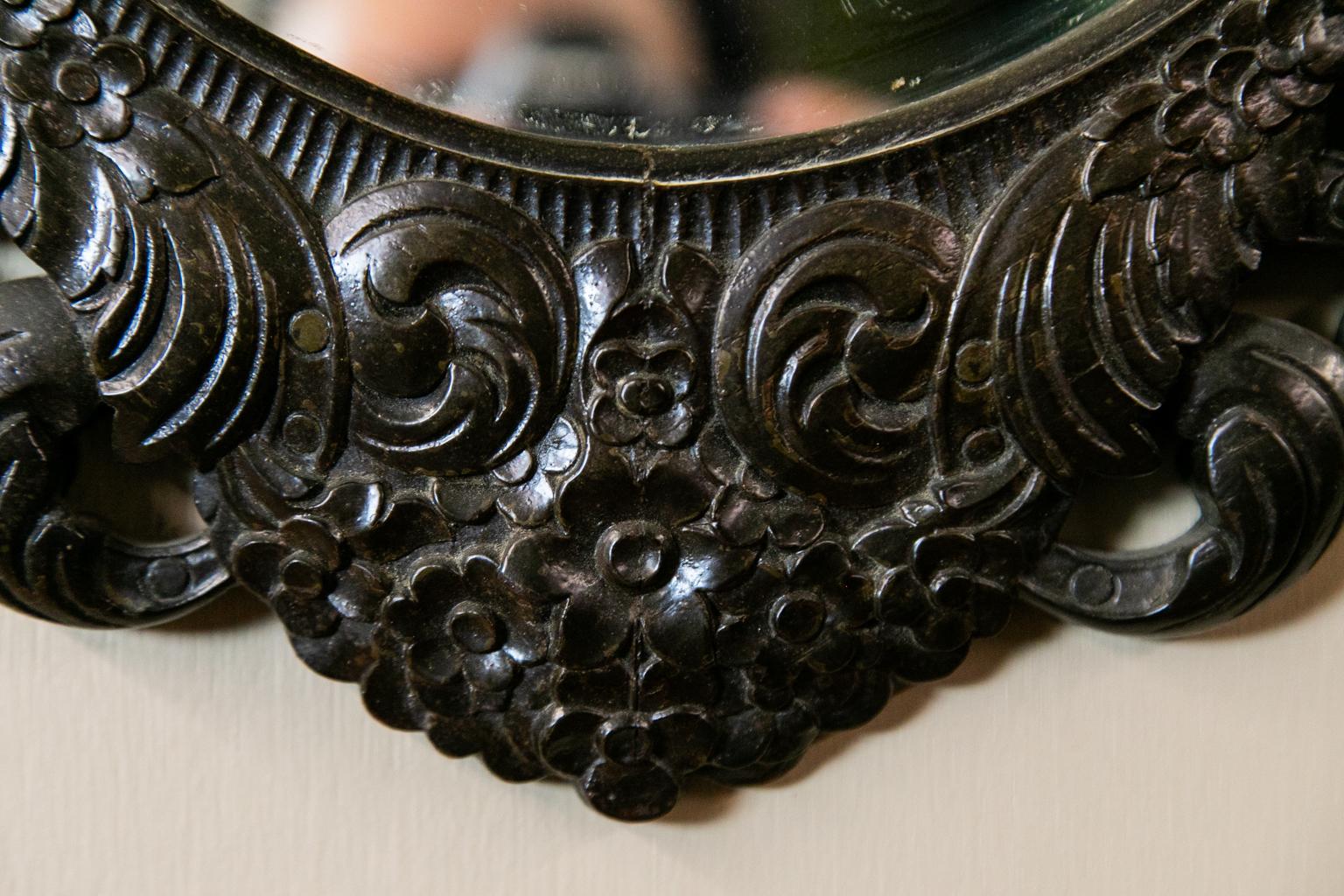 Carved English oval mirror has a floral basket in the crest and leaf arabesques and flowers in the frame.
 