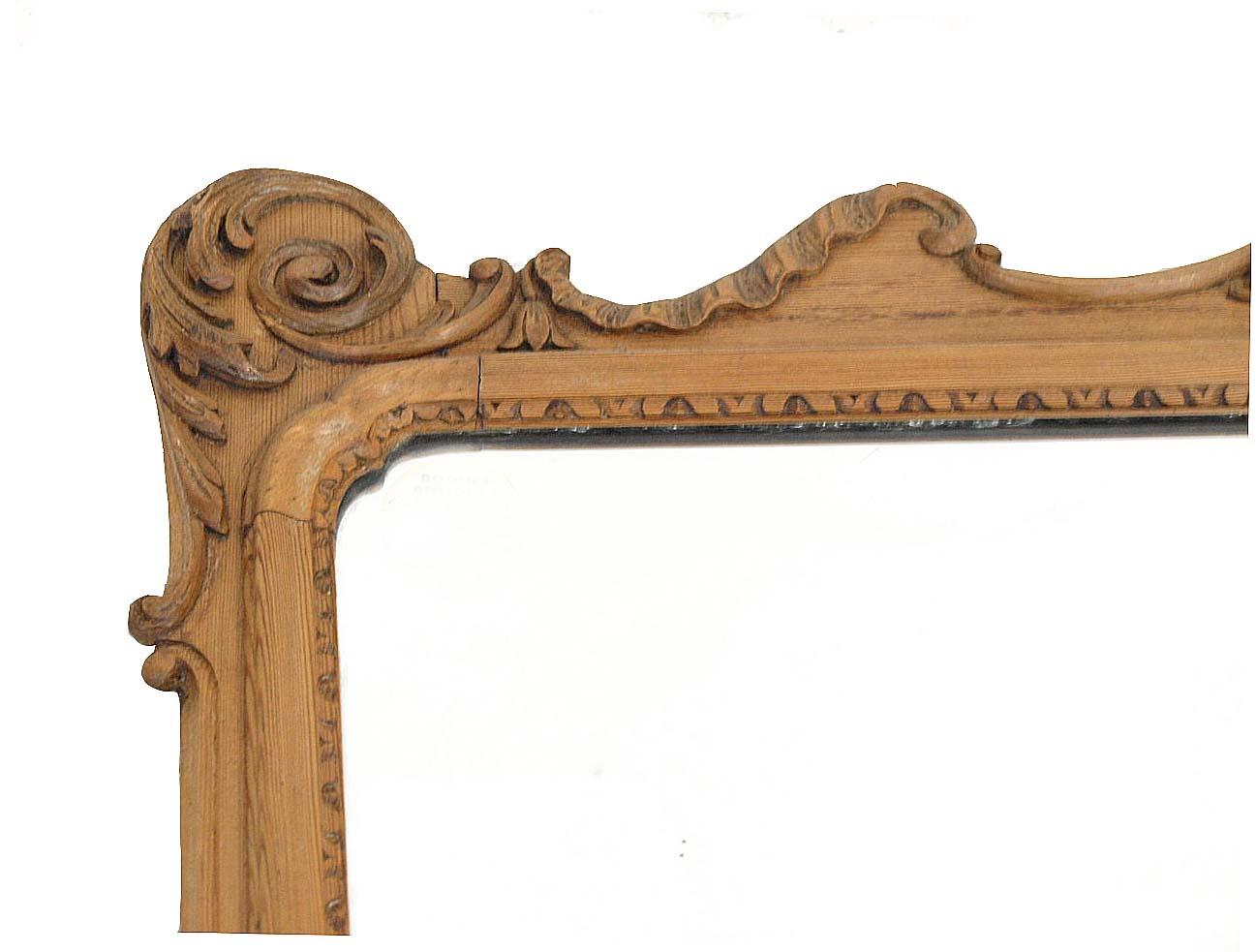 Carved English pine horizontal mirror featuring a variety of architectural carvings in high relief; the top portion with broken arch and demi lune platform above oval carved medallion; bottom portion with central carved shell flanked by small