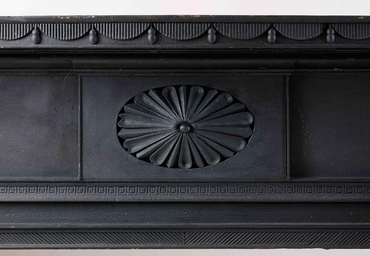 New York, circa 1818

The shaped mantle shelf with applied tambour drapery swags on its front edge, above a cove molding above a frieze with a central fan-carved oval rosette above a framed fire box opening, flanked on the jams by corbels