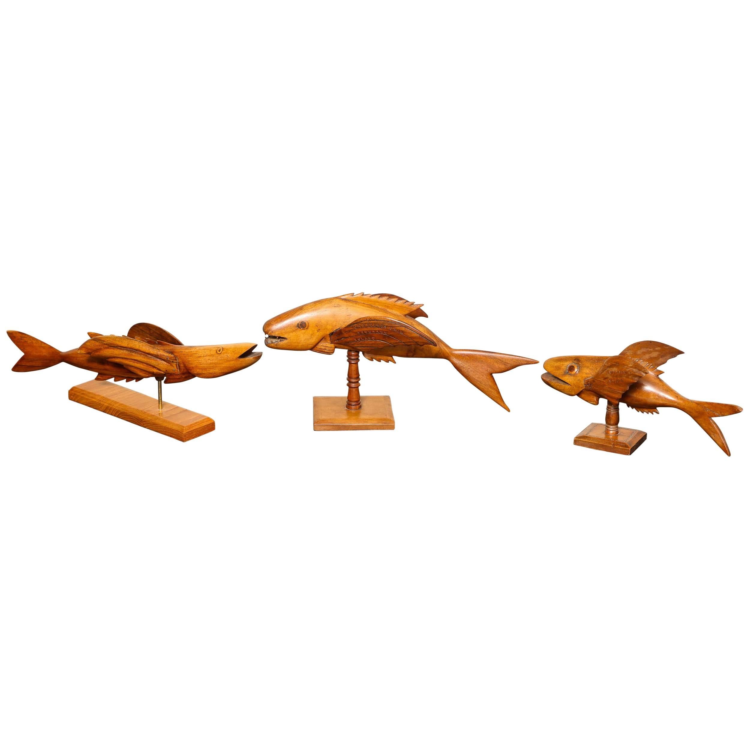 Poissons volants (trois disponibles) sculptés en bois exotique ayant des ailes et montés sur des supports. Différentes formes et tailles:: comme indiqué. Chacune est estampillée Pitcairn Island:: l'une est signée Lancy Christian:: et une autre Len
