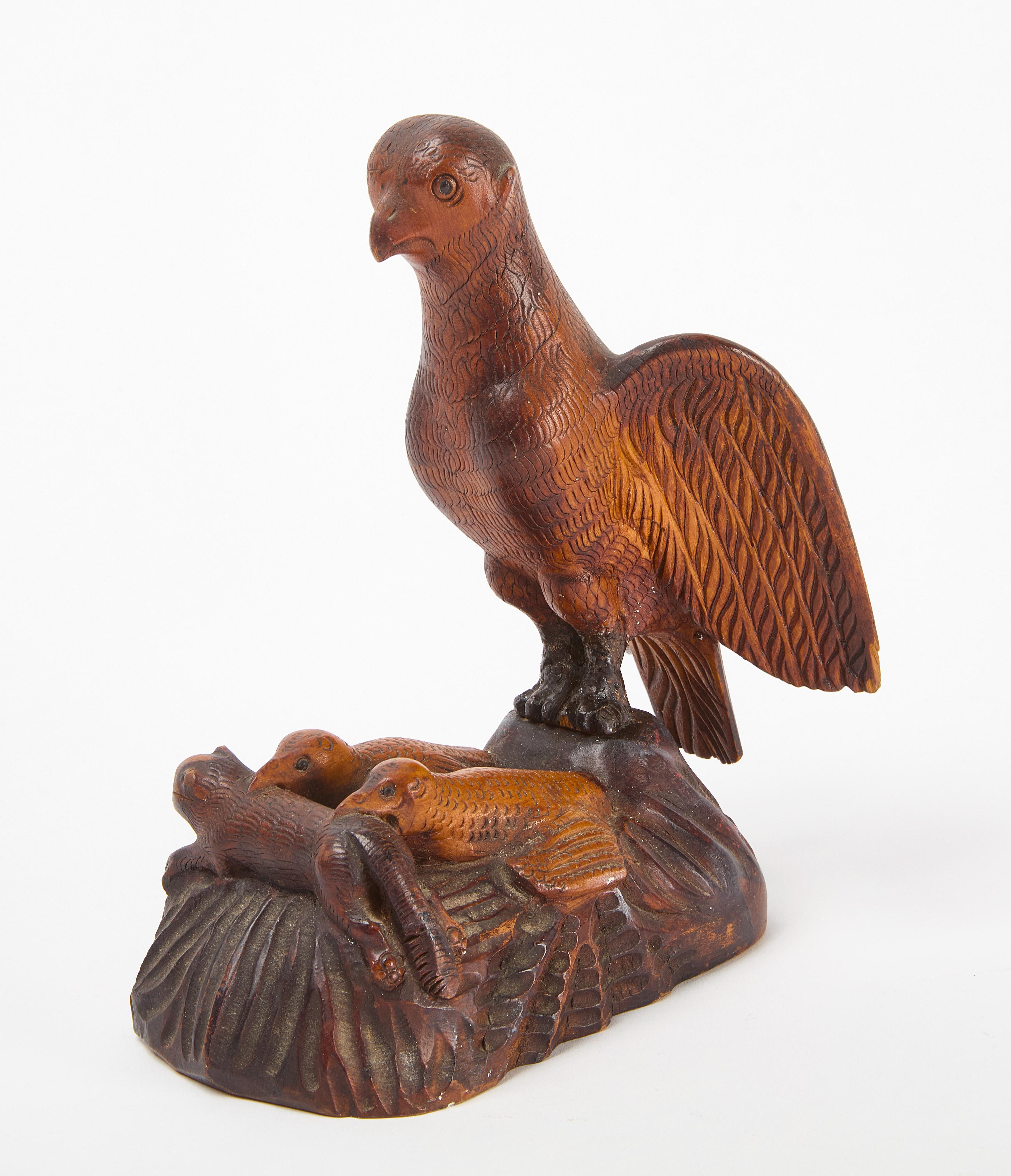 Figure sculptée d'art populaire représentant une mère aigle surveillant deux aiglons et un chien. En dessous se trouvent une porte coulissante et un compartiment 