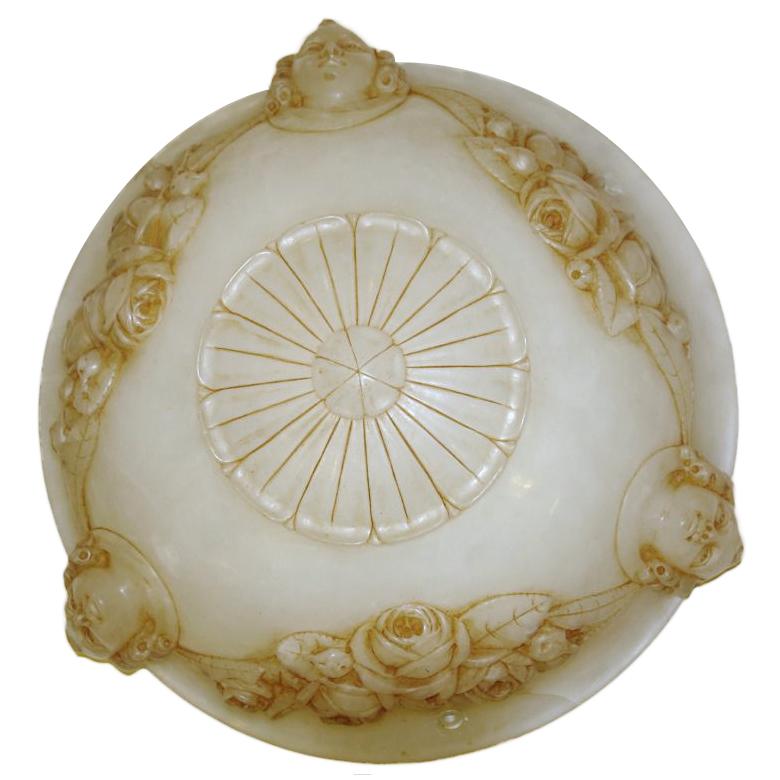 A carved alabaster light fixture with garlands of flowers and putti faces with interior lights; to be fitted with bronze chain and canopy.

Measurements:
Depth of bowl: 6
