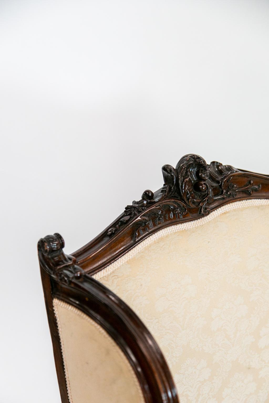 This carved French slipper armchair has detailed carving all-over using floral and leaf motifs. The front has a serpentine apron and the cabriole legs terminate in scrolled feet. It has been recently reupholstered in an ivory damask.