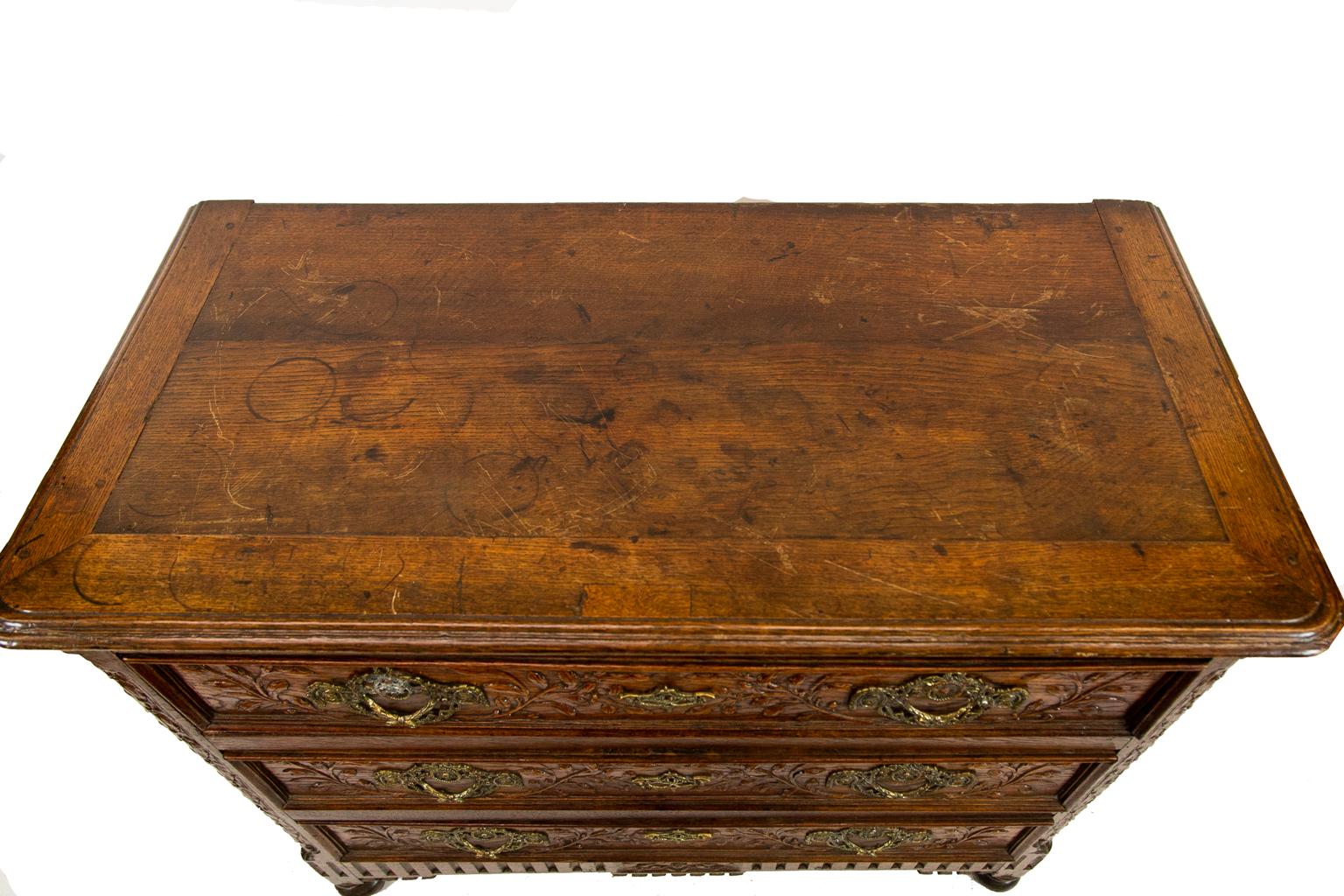 Carved French three-drawer commode, the drawers carved in high relief with leaf and berry carvings. The base apron is fluted and has carved tassels. The sides are raised paneled, while the front and back corners have leaf and berry carvings, on