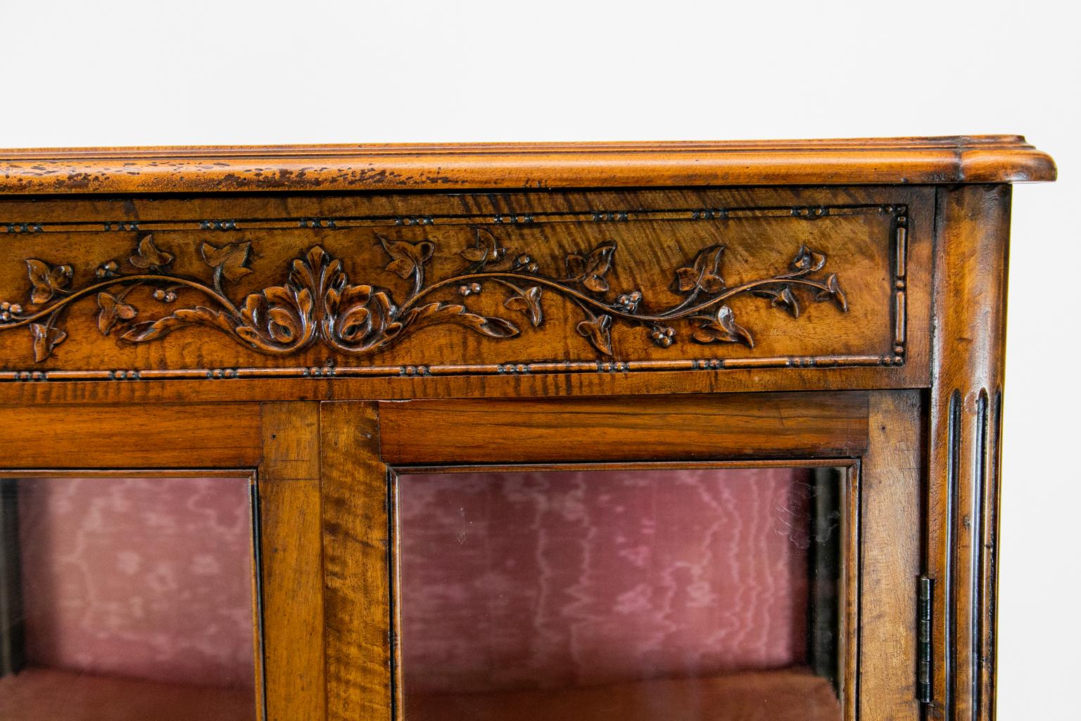 Carved French walnut display cabinet, the frieze carved with floral grapevine arabesques. The lower doors have raised panels carved with mandolins, flutes, and branches. The apron has carved molding with a floral center. Diapering stiles are fluted
