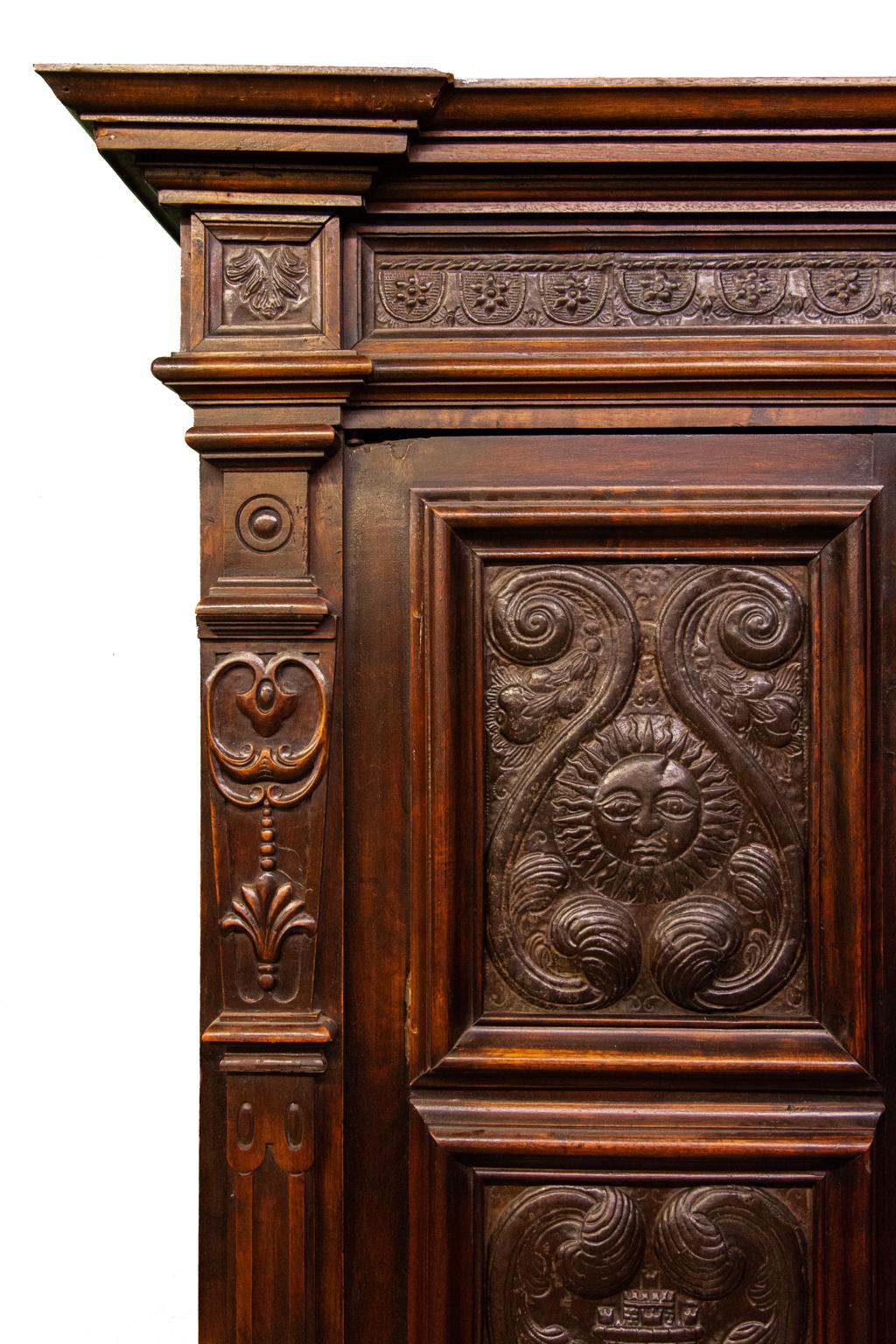 Carved French walnut punched tin cabinet, with deep cornice above tin lined frieze, above double doors each with tin panels depicting a man in the moon, a sun, baskets, castles, and palm trees, sides also with tin panels. Lower section with carved