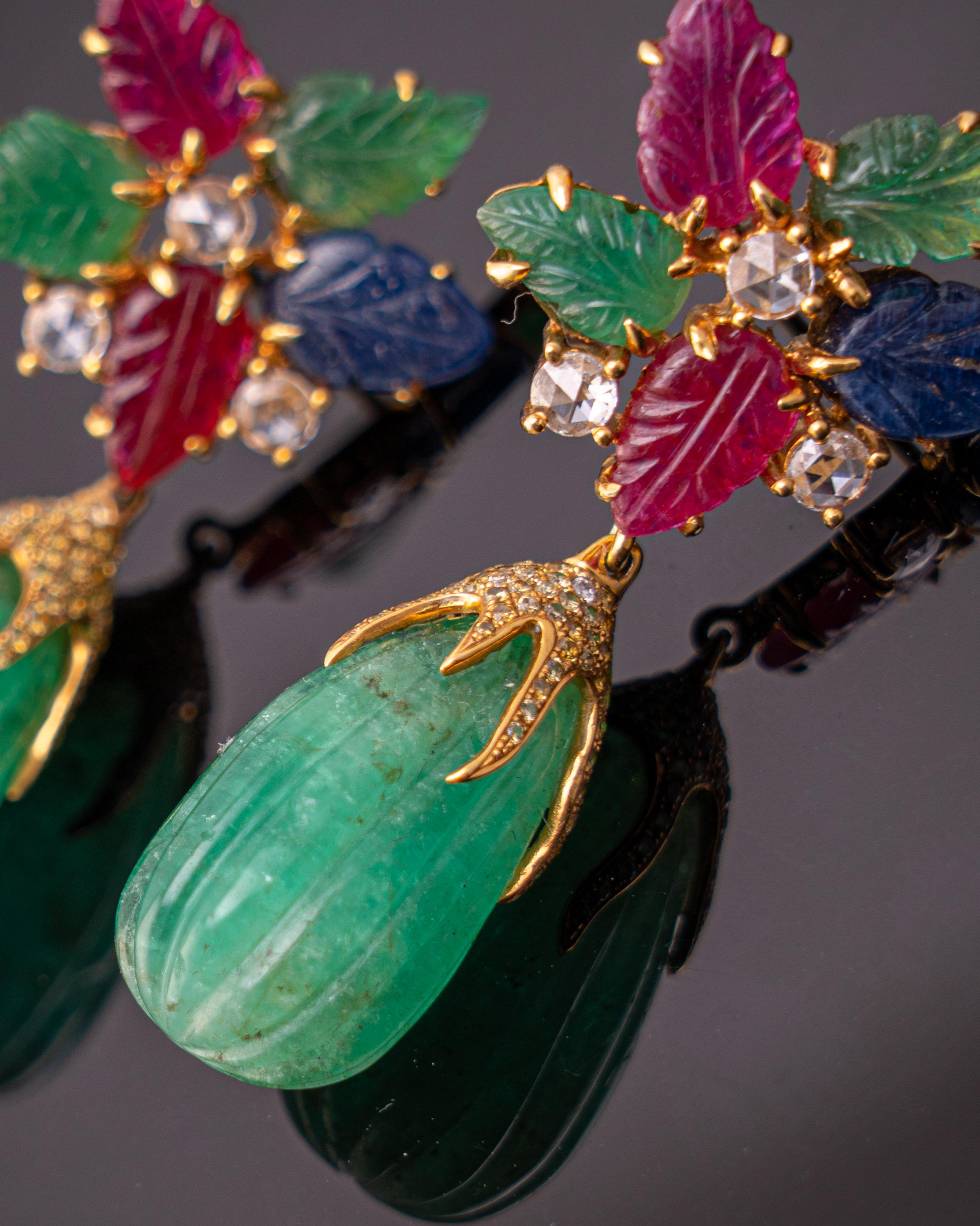 A pair of earrings, with carved natural Burmese Rubies, Colombian Emeralds and Blue Sapphire. This pair looks very Art-Deco, as each stone is very unique. Push-pull backing is used, and the stones are set in solid 18K Yellow Gold. The earrings are