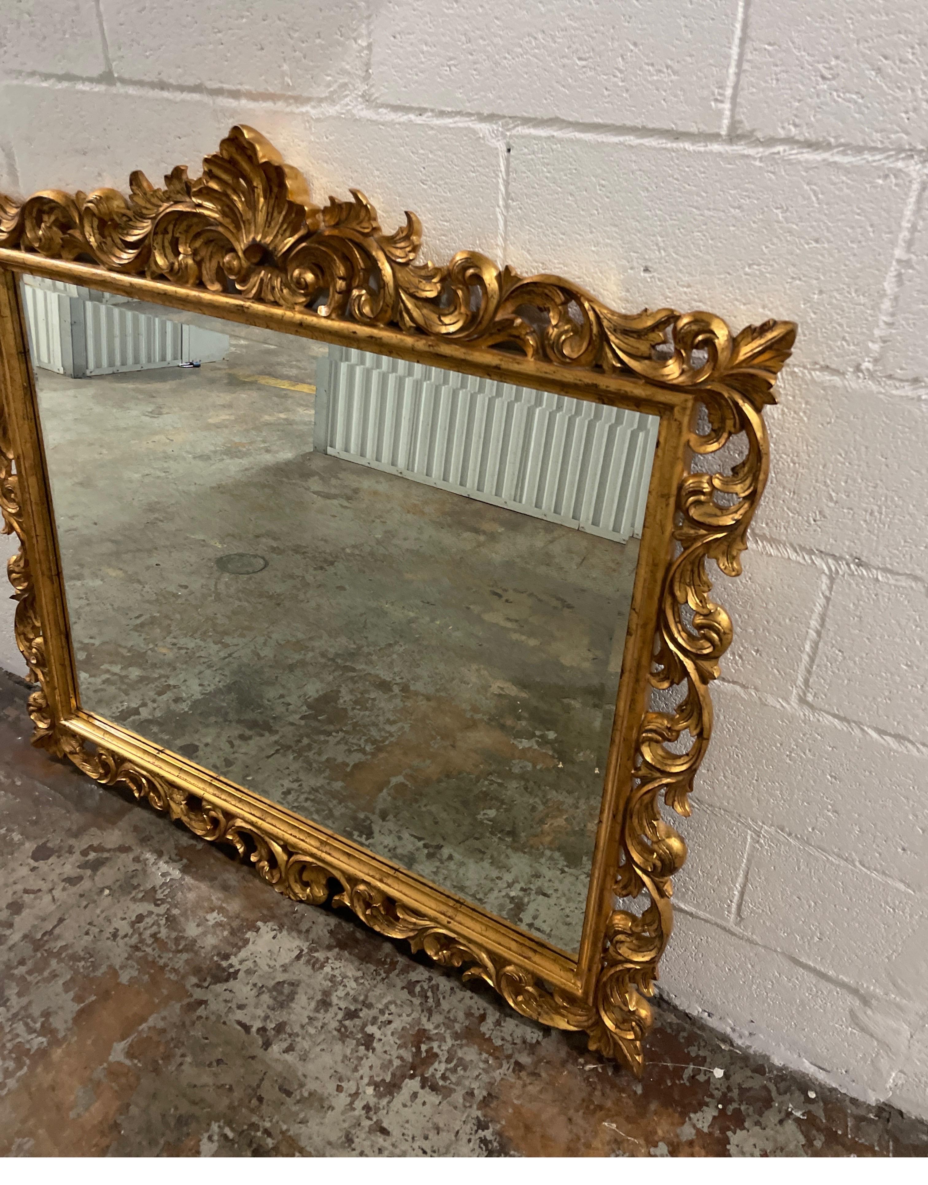 Hand carved & gilded over mantel mirror by Harrison & Gil for Dauphine Mirror Co. This beautiful gilded baroque mirror is topped with a fleur de lys.