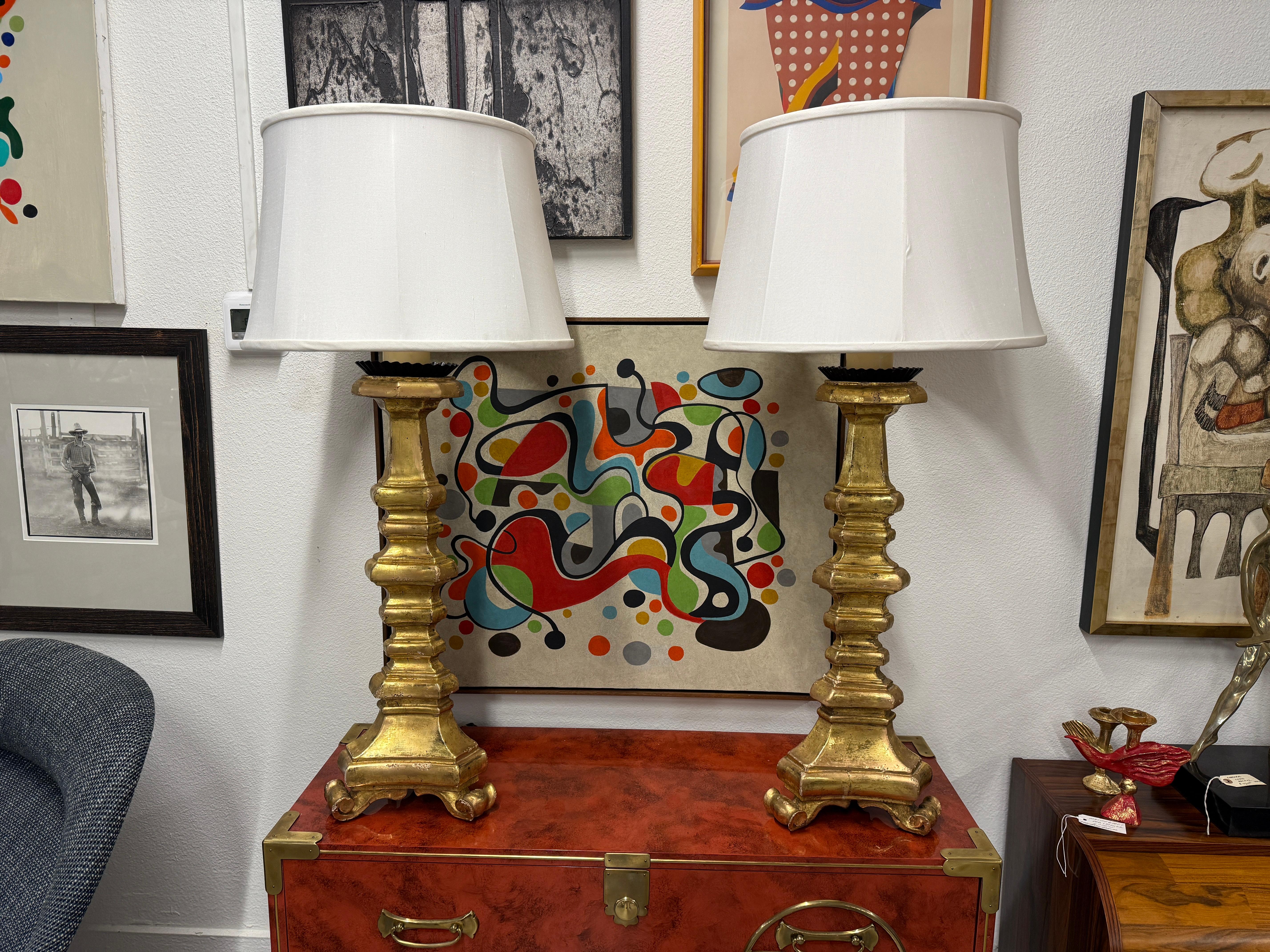 A nice pair of giltwood carved Italian lamps. These lamps are beautifully gilded and nicely carved. They feature double dark brass clusters fittings and nicely silk shades. The lamps are in working order. 
The lamps have been retouched at some point