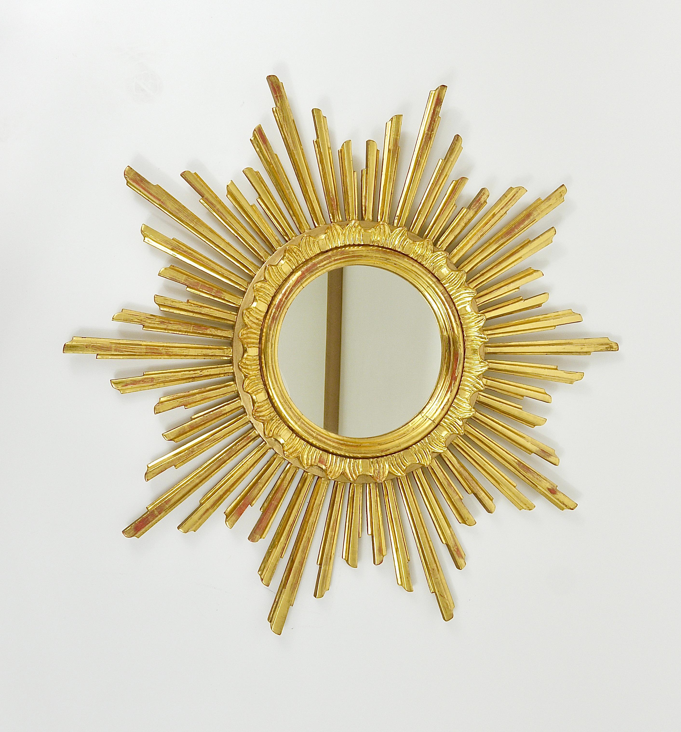 A beautiful, large golden mid-century soleil sunburst starburst gilt wood mirror. Made in France, dated around the 1960s. Handmade of carved gold-plated wood, in good condition. Total diameter 27“, the diameter of the mirror itself is 8“.