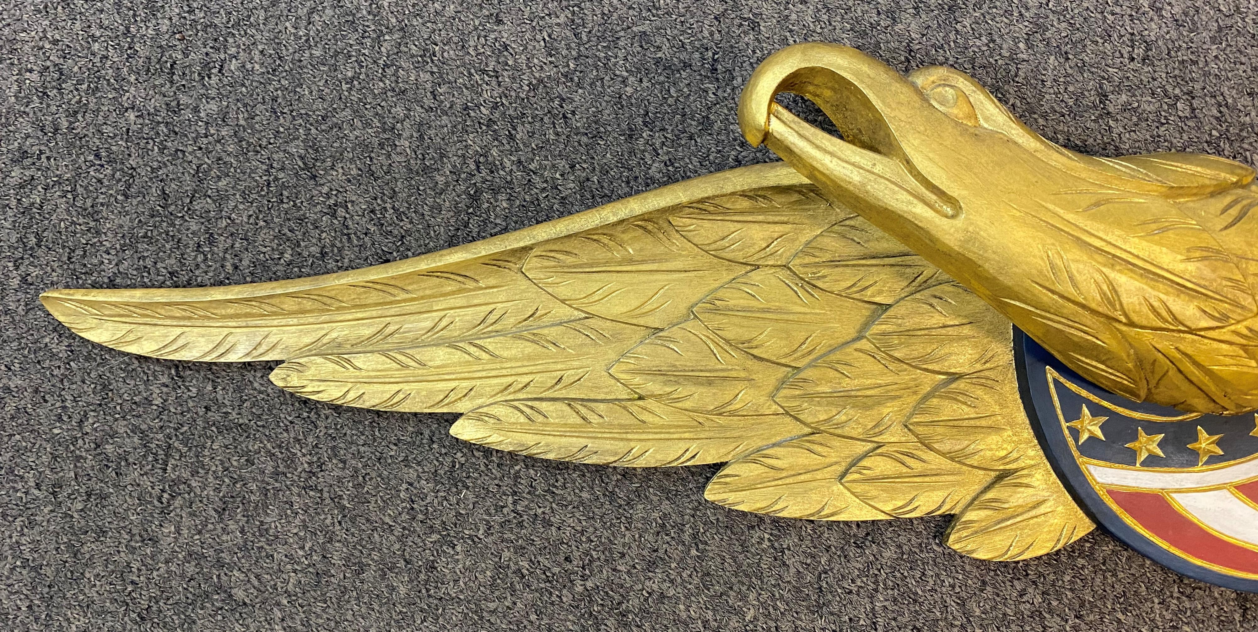 A finely detailed hand carved and gilt wooden Bellamy style eagle wall plaque with painted American flag shield decoration by contemporary Cape Cod artist Paul White. White is from East Sandwich, Massachusetts and is among the most respected and