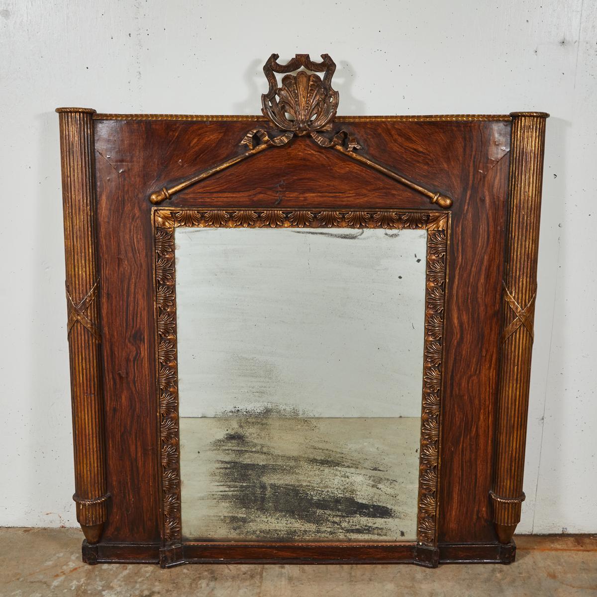 Dramatic early 19th-century carved and gilt wood mirror with painted faux bois accents from France.  Flanked on either side by two reeded columns with conical finial bases, the mirror features a palmette motif border and pediment crowned by a crest