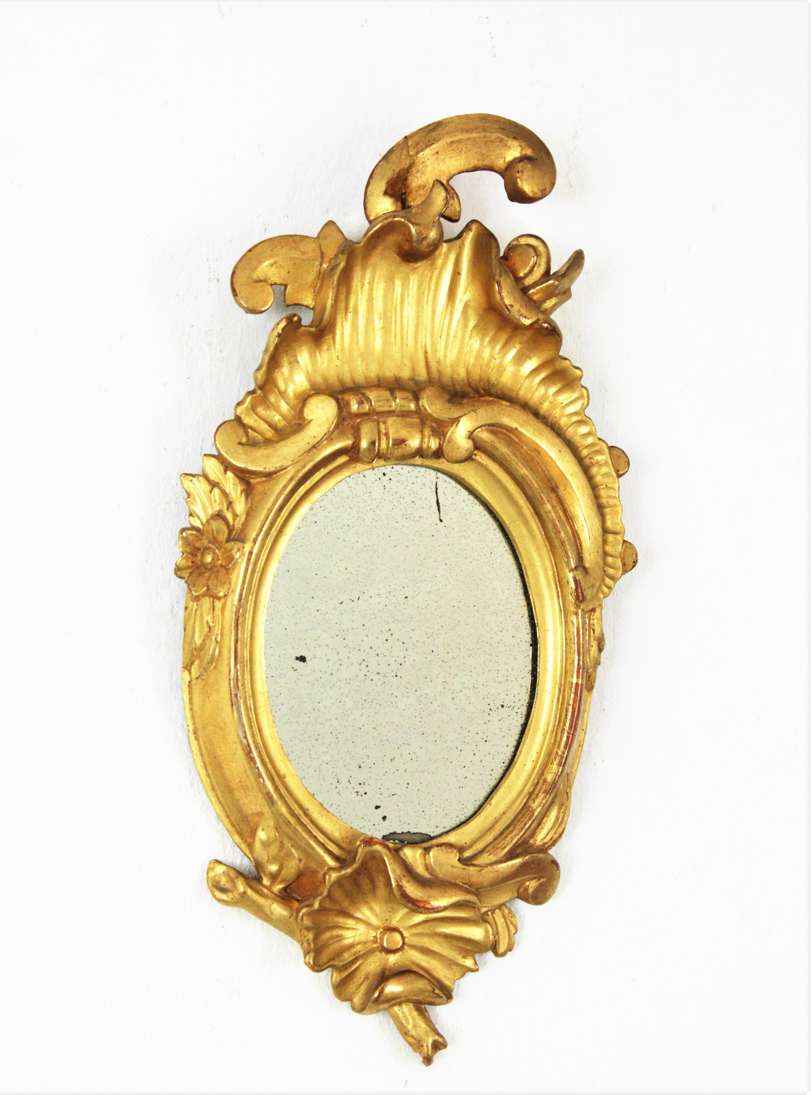 Specchio in miniatura in legno dorato con stemma, Spagna, anni '20
Specchio ovale finemente intagliato con cresta. Legno intagliato, ricoperto di gesso, finitura in foglia d'oro a 24 carati. 
Questo specchio intagliato Art Carved di piccole