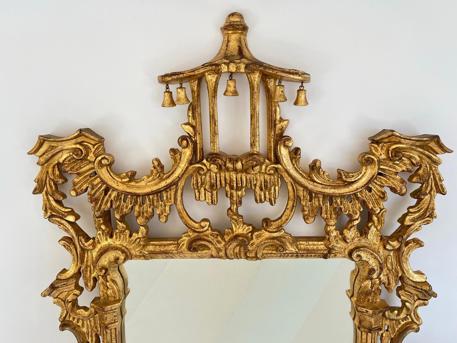 Miroir mural en bois doré sculpté, de style Brighton Pavilion, présentant un cadre élaboré, sculpté à la main et percé, surmonté d'un fronton en forme de pagode, et garni de clochettes en bois, son cadre étant entouré de volutes en forme de C et de