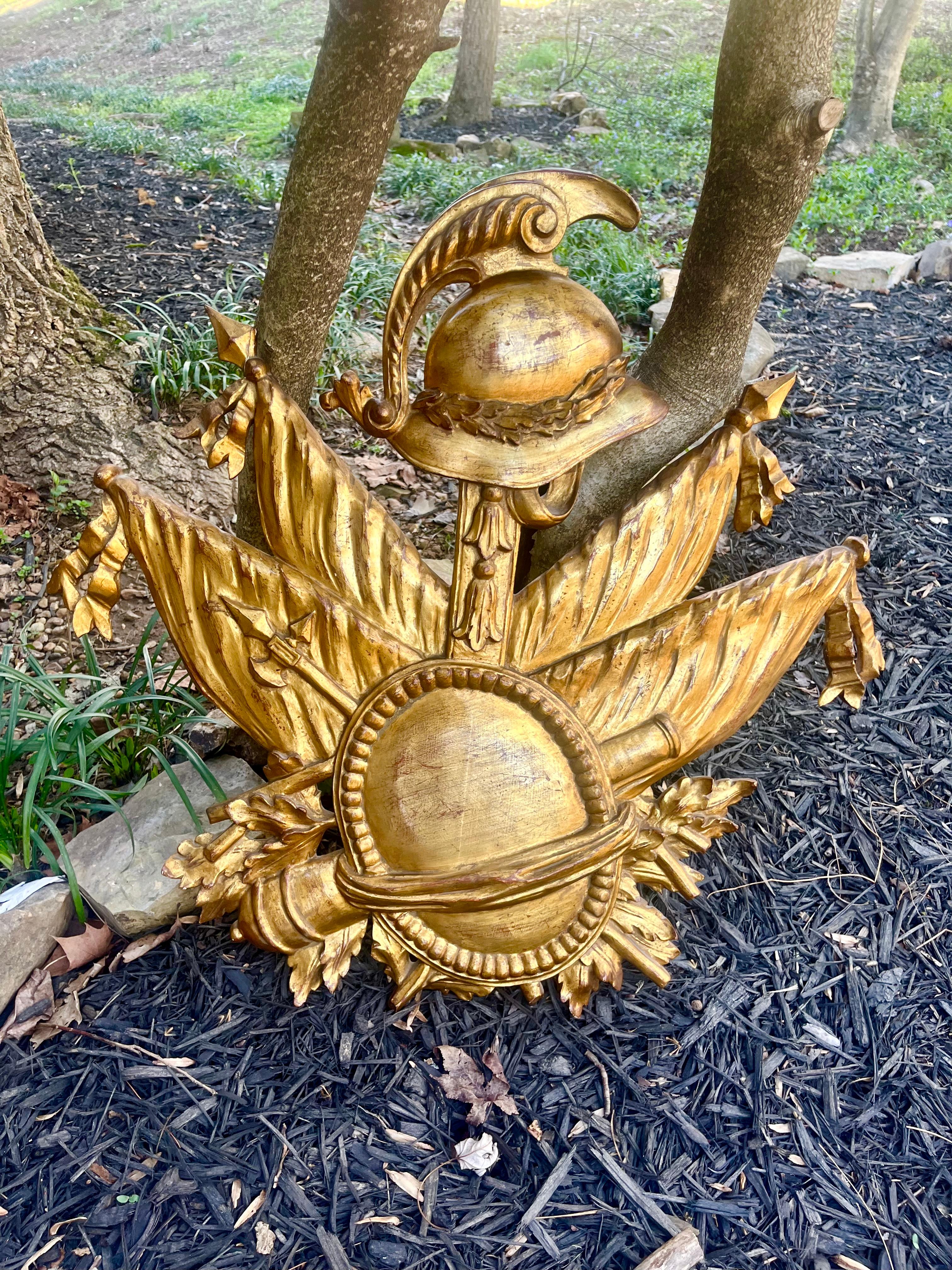 Presents very well  with crisp and well defined carving  . A Giltwood wall carved  trophy. The banners tilt out  , with center helmet and shield .Of military inspiration against background of banners and military accessories .
Sturdy and stable