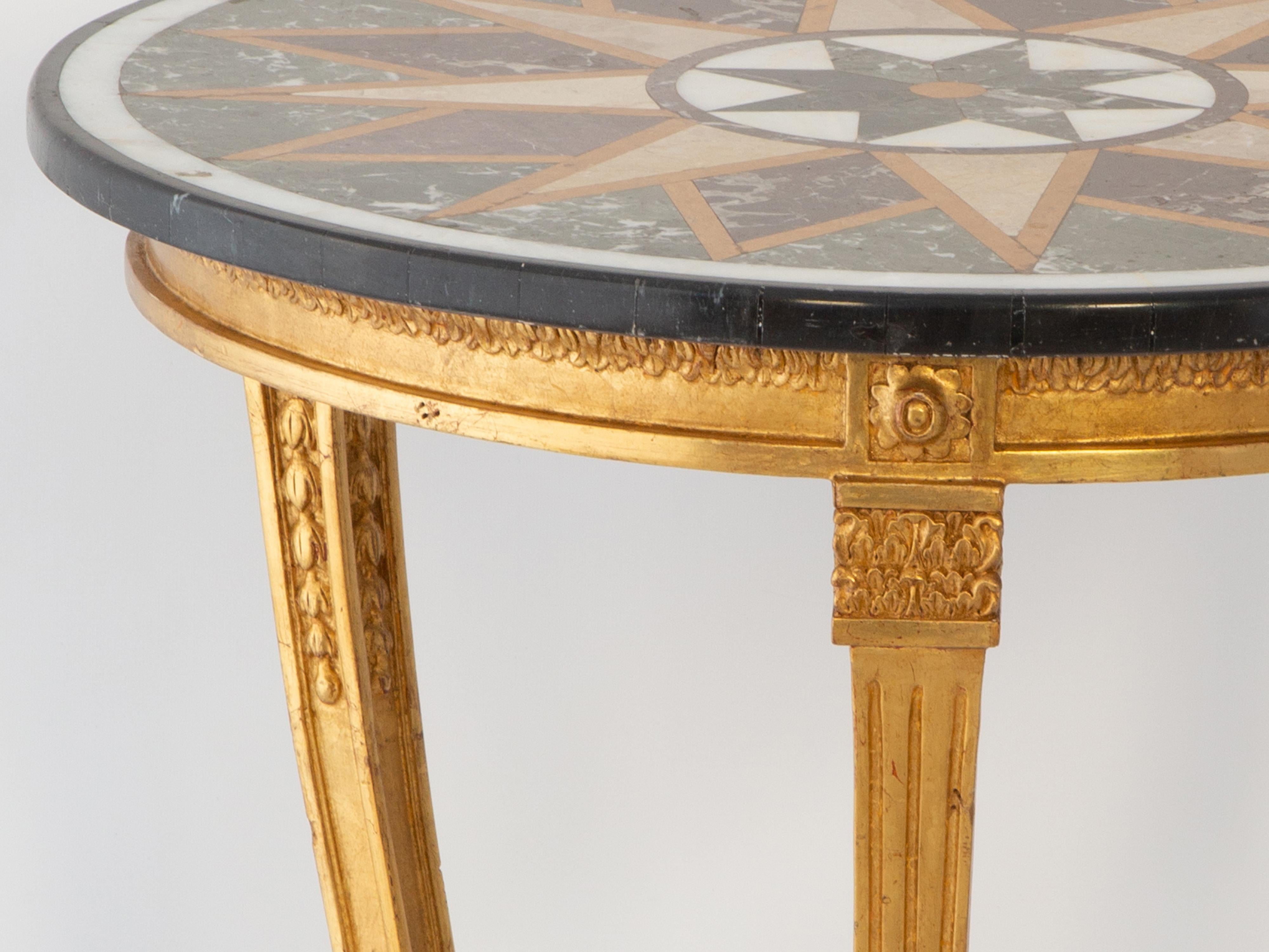Table d'appoint en guéridon, avec un plateau rond antique en pietra dura, incrusté d'un motif en forme d'étoile. Sa base de table plus tardive, en bois doré sculpté, avec un tablier cannelé, est décorée de godrons. Elle repose sur trois pieds